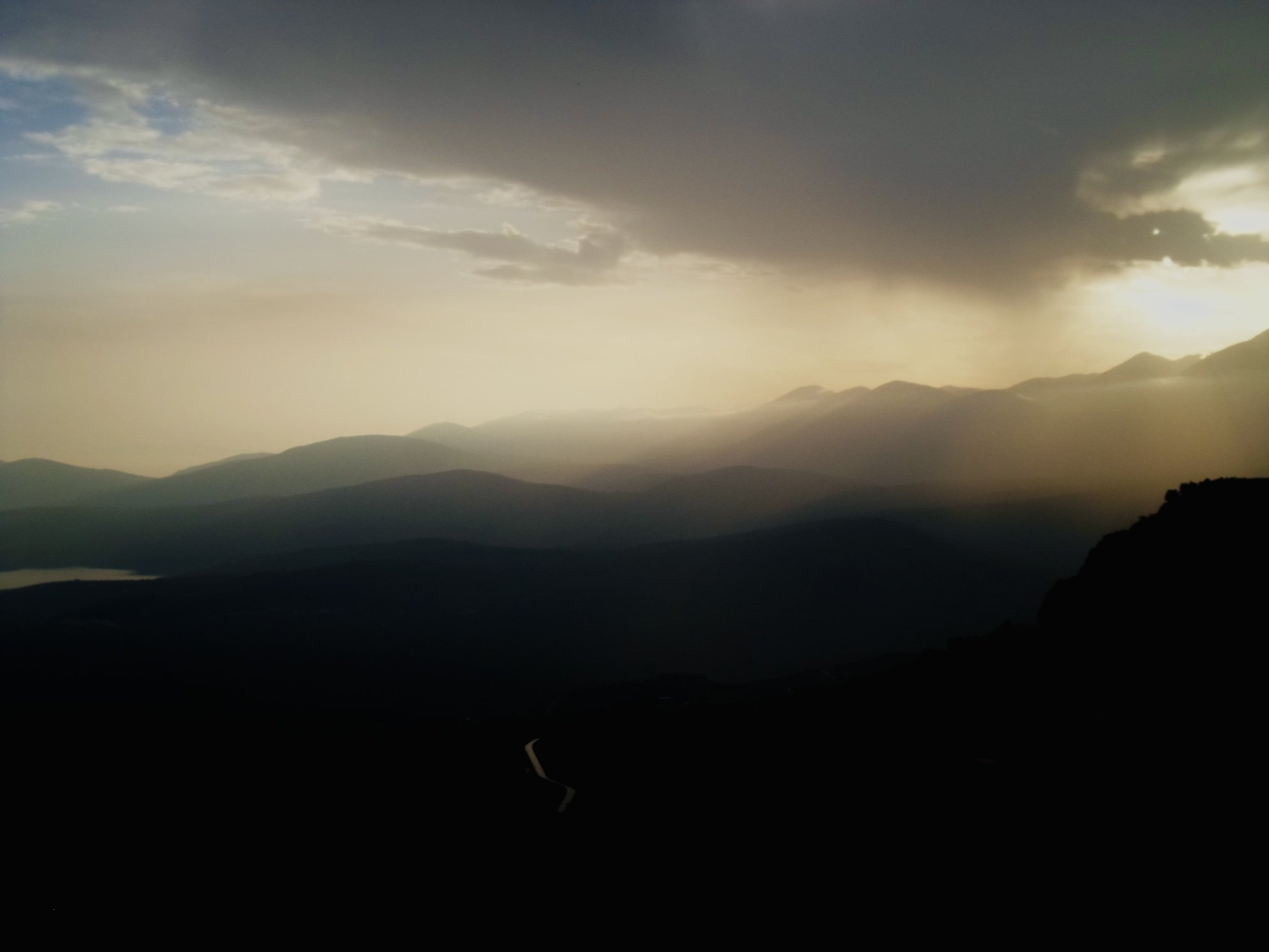 A scenic mountain landscape at sunset with dark clouds overhead and layers of mountains fading into the distance.