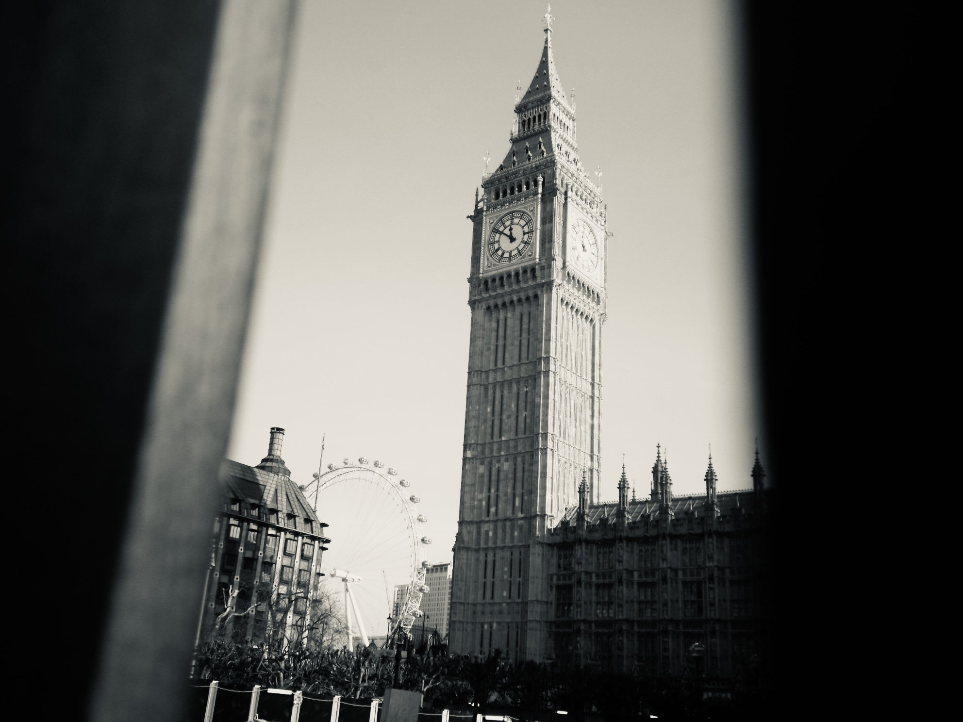 Black and white photo of Big Ben clock tower in London, with a partially visible Ferris wheel and other buildings in the background.