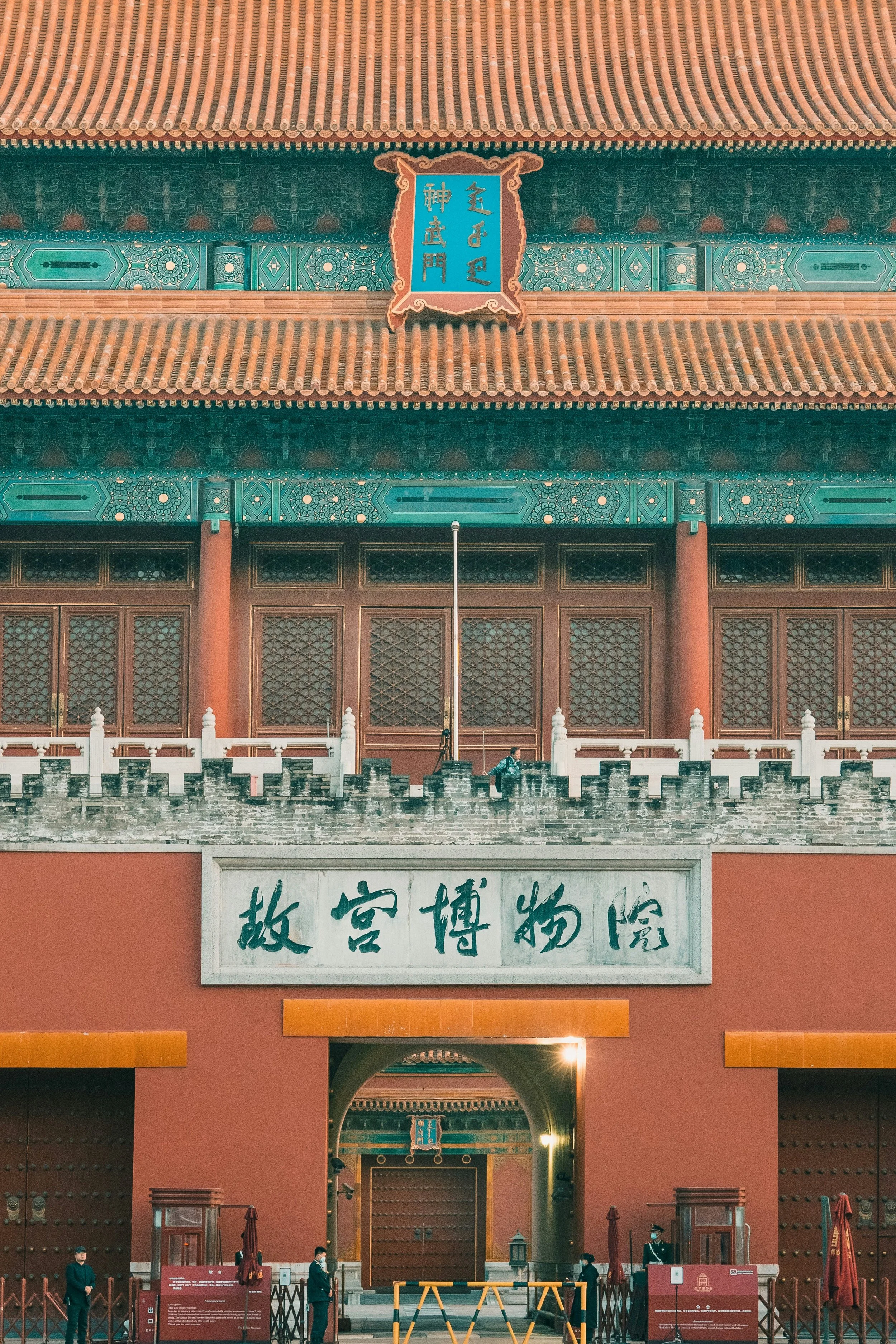The entrance of the Palace Museum in Beijing, China, with traditional Chinese architecture, large wooden doors, Chinese characters sign, and guards.
