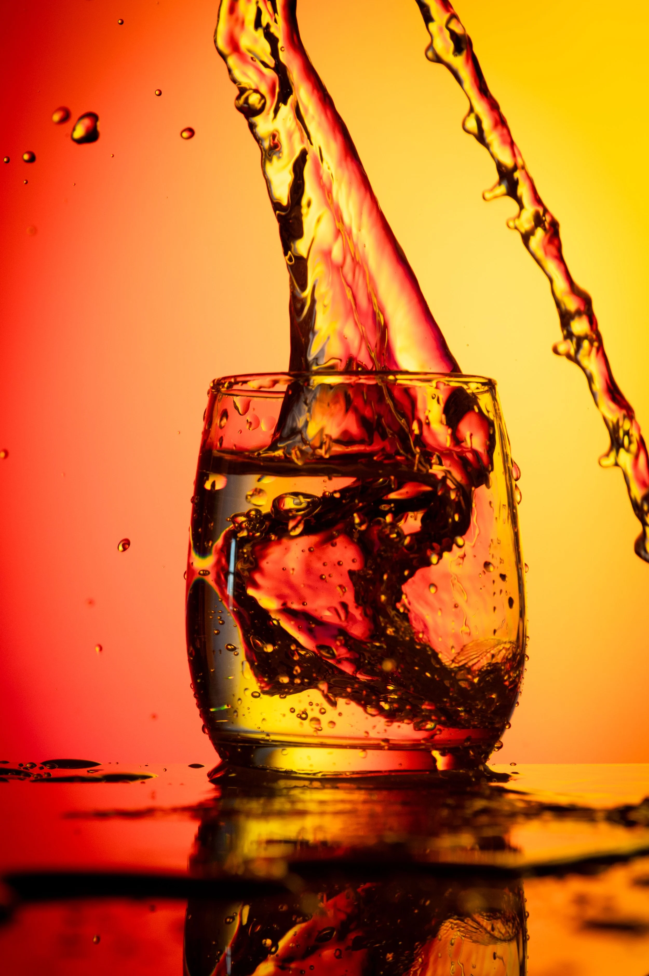 A glass of water with ice cubes being filled with a clear liquid, with a warm orange and yellow gradient background.