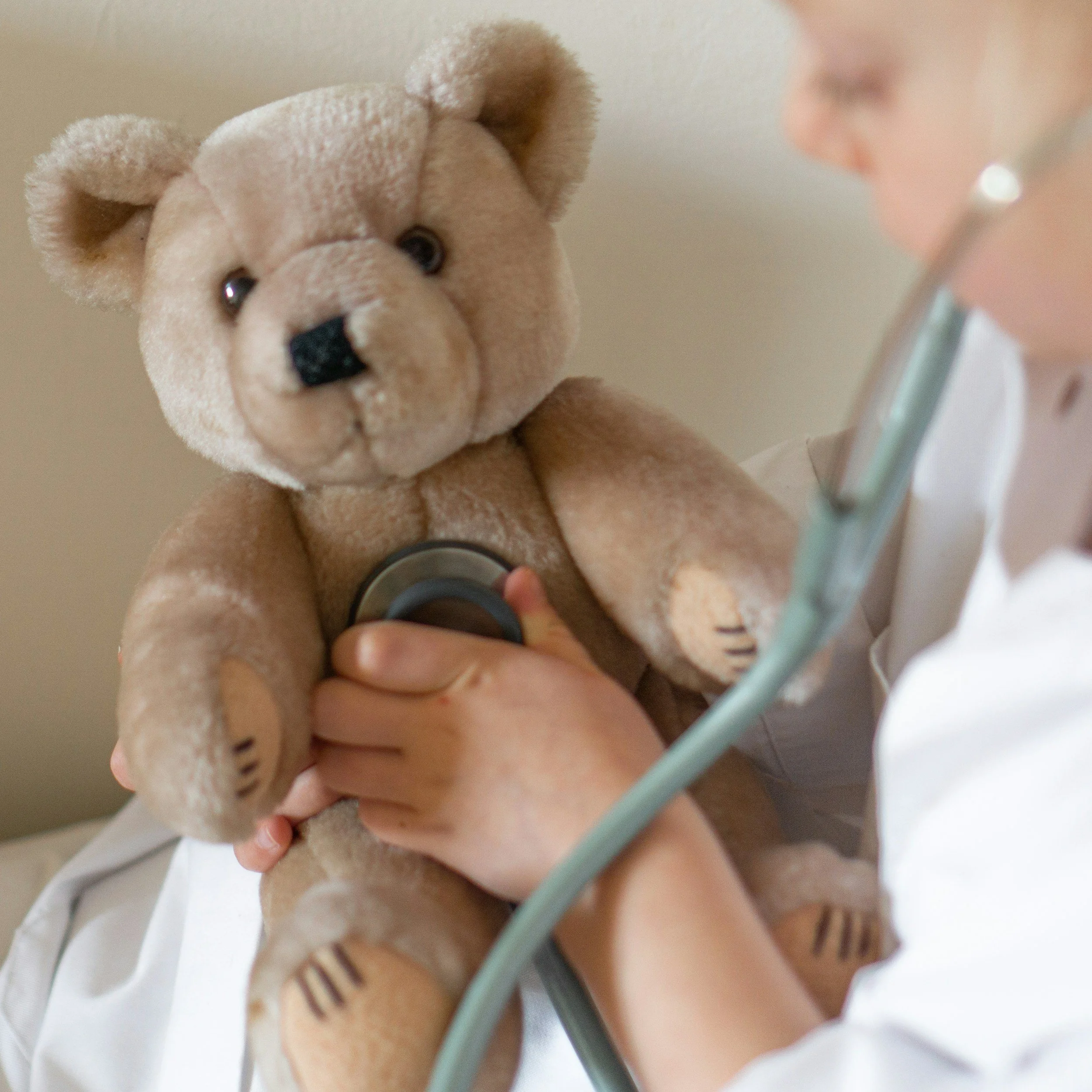 A person in a white coat holding a teddy bear with a stethoscope on its chest, as if diagnosing it.