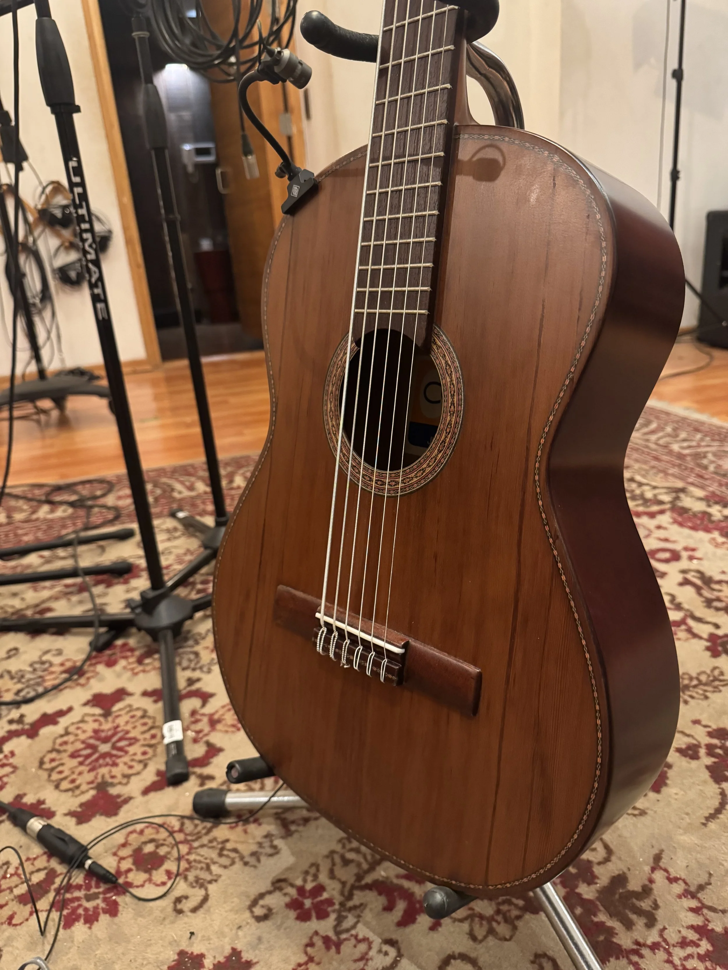 An acoustic guitar on a stand with recording equipment in a music studio setting.
