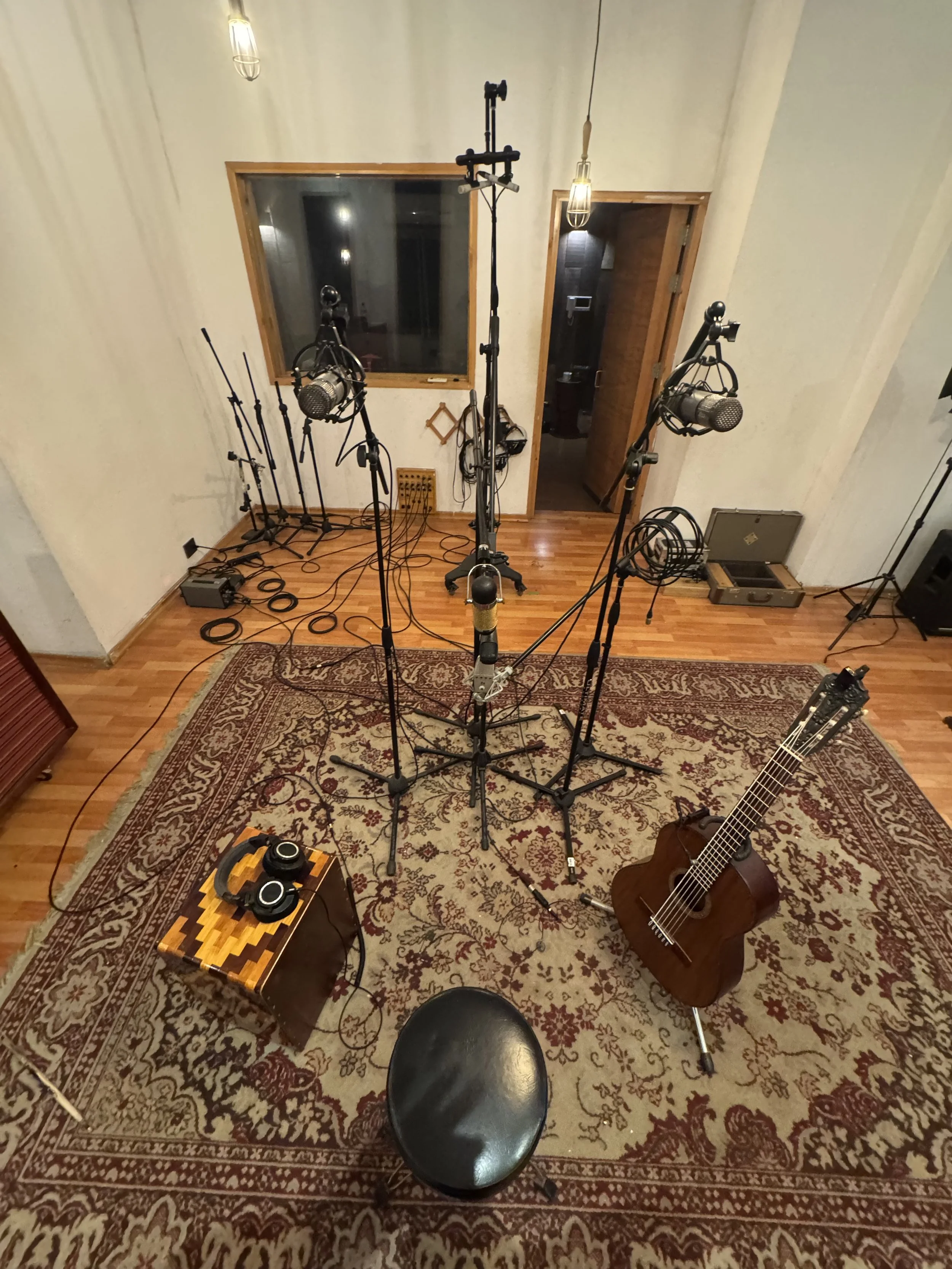 Recording studio room with microphones, a guitar, headphones, and a chair on a patterned rug.