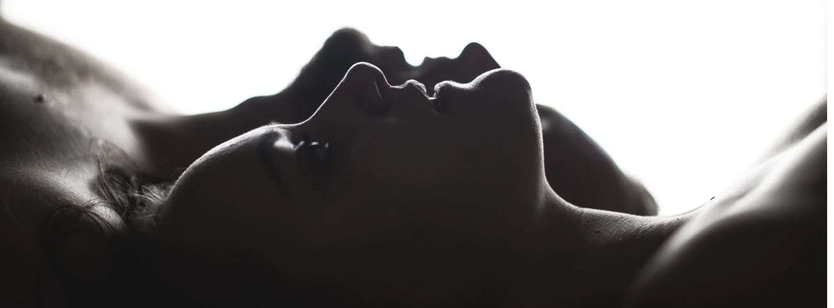 Silhouettes of two women lying down facing each other, with their faces close together, backlit to create a dramatic shadowed effect.