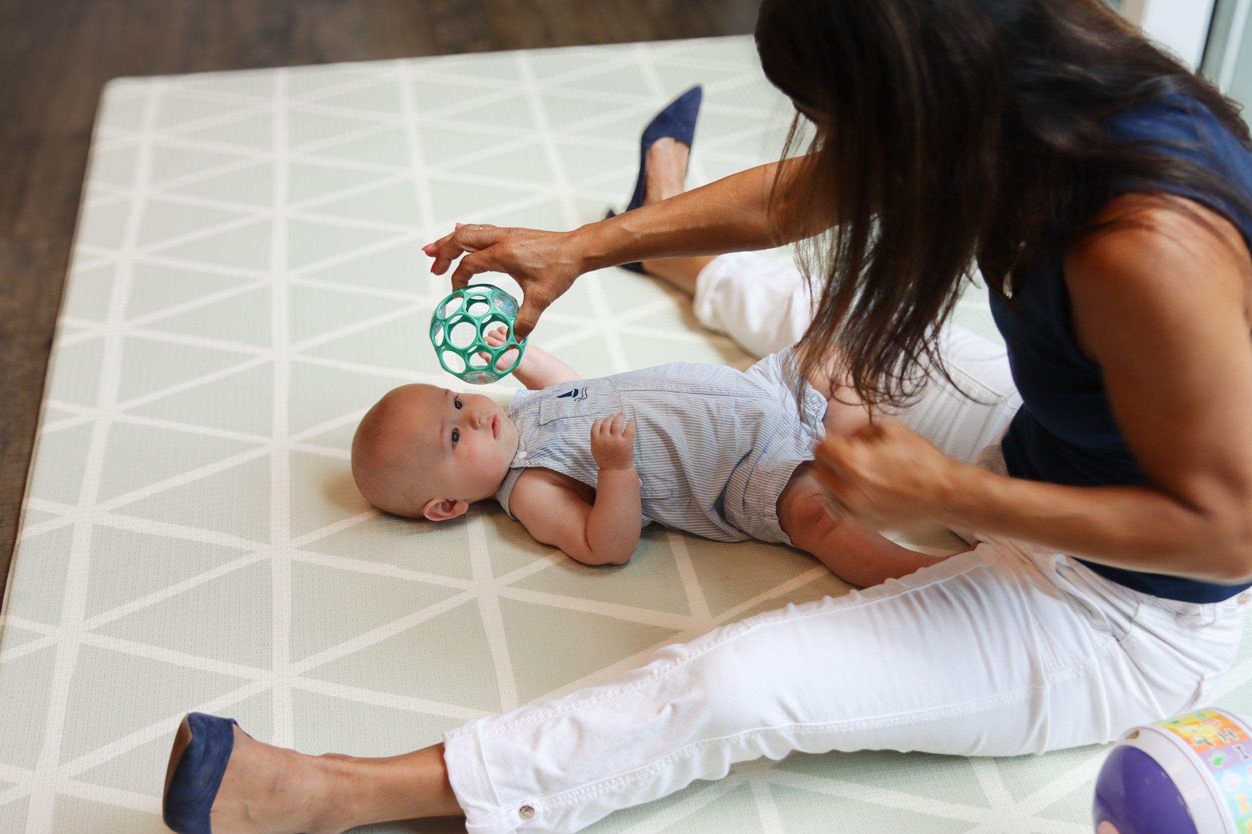 A baby lays on a mat and looks at a ball that Andrea Callanen holds.