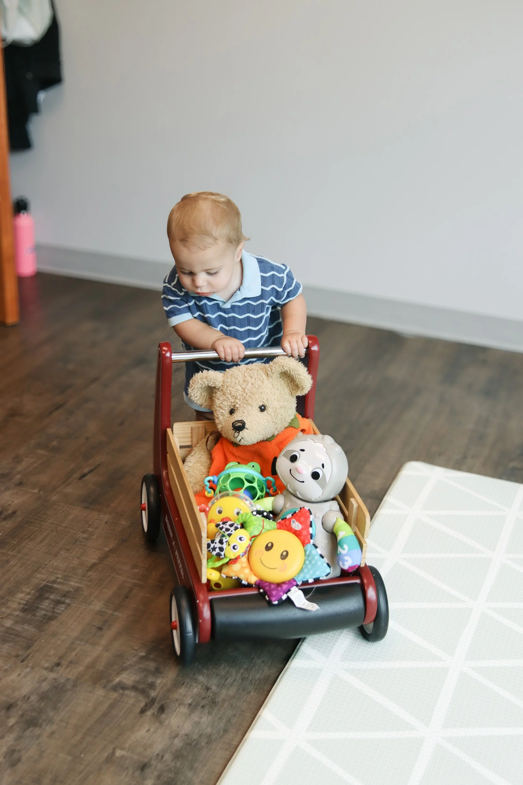 A baby walks in the Looking Ahead Pediatric Therapies office, pushing a wagon of toys.