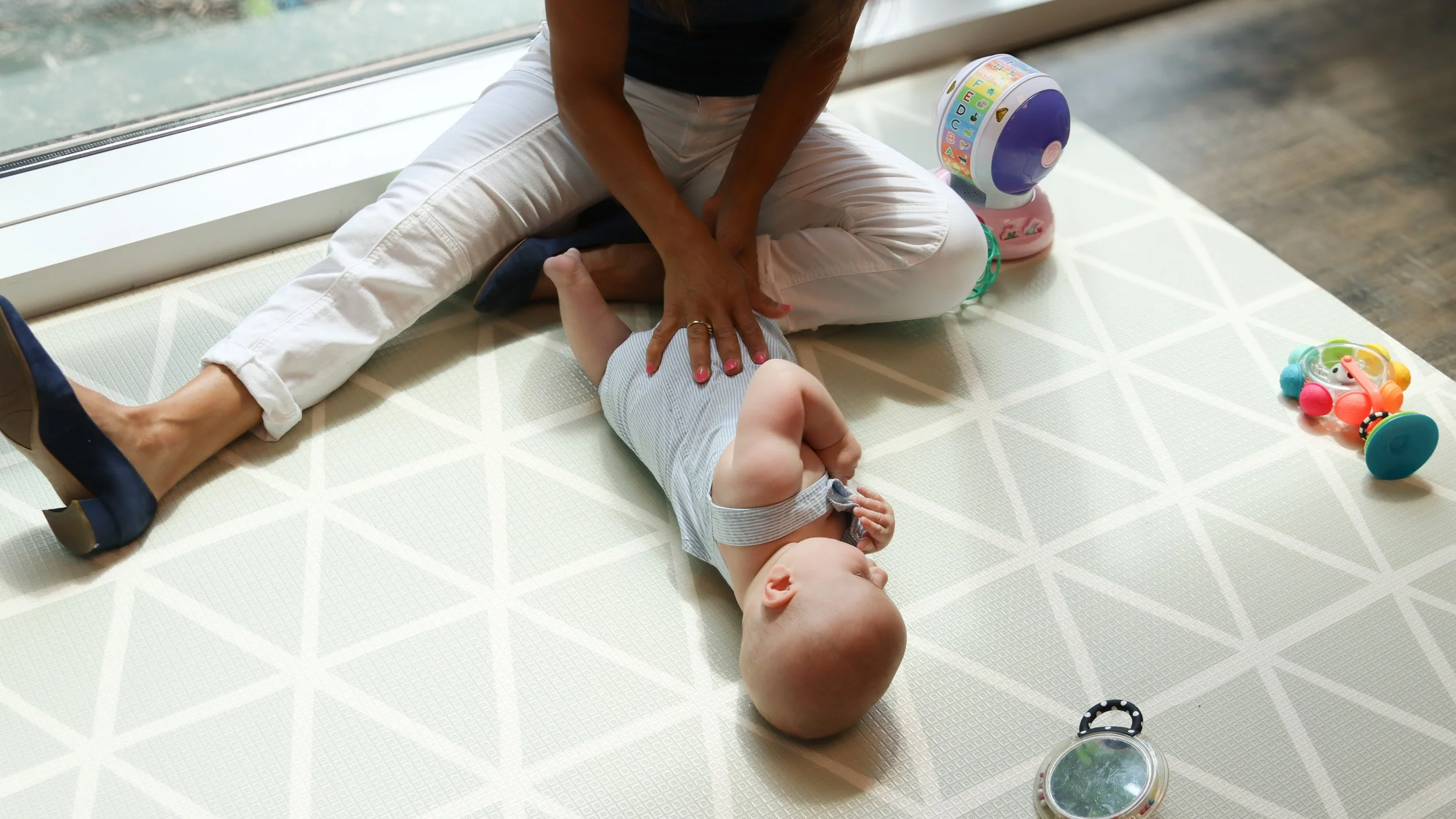 Andrea Callanen sits on the floor with a baby with torticollis and works on his ability to roll