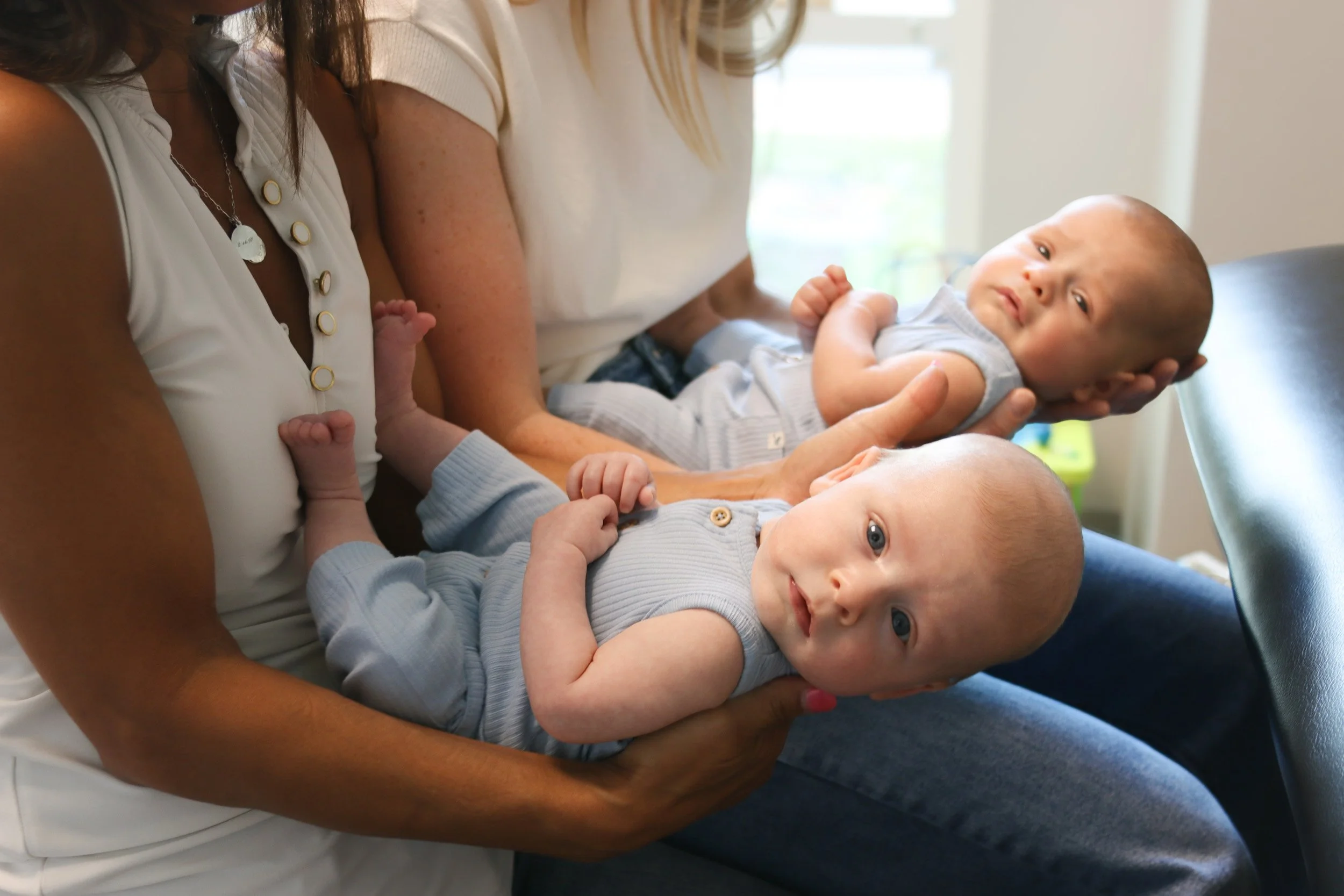 Twin boys look at the camera, as they are held by two pediatric physical therapist who specialize in torticollis and plagiocephaly care