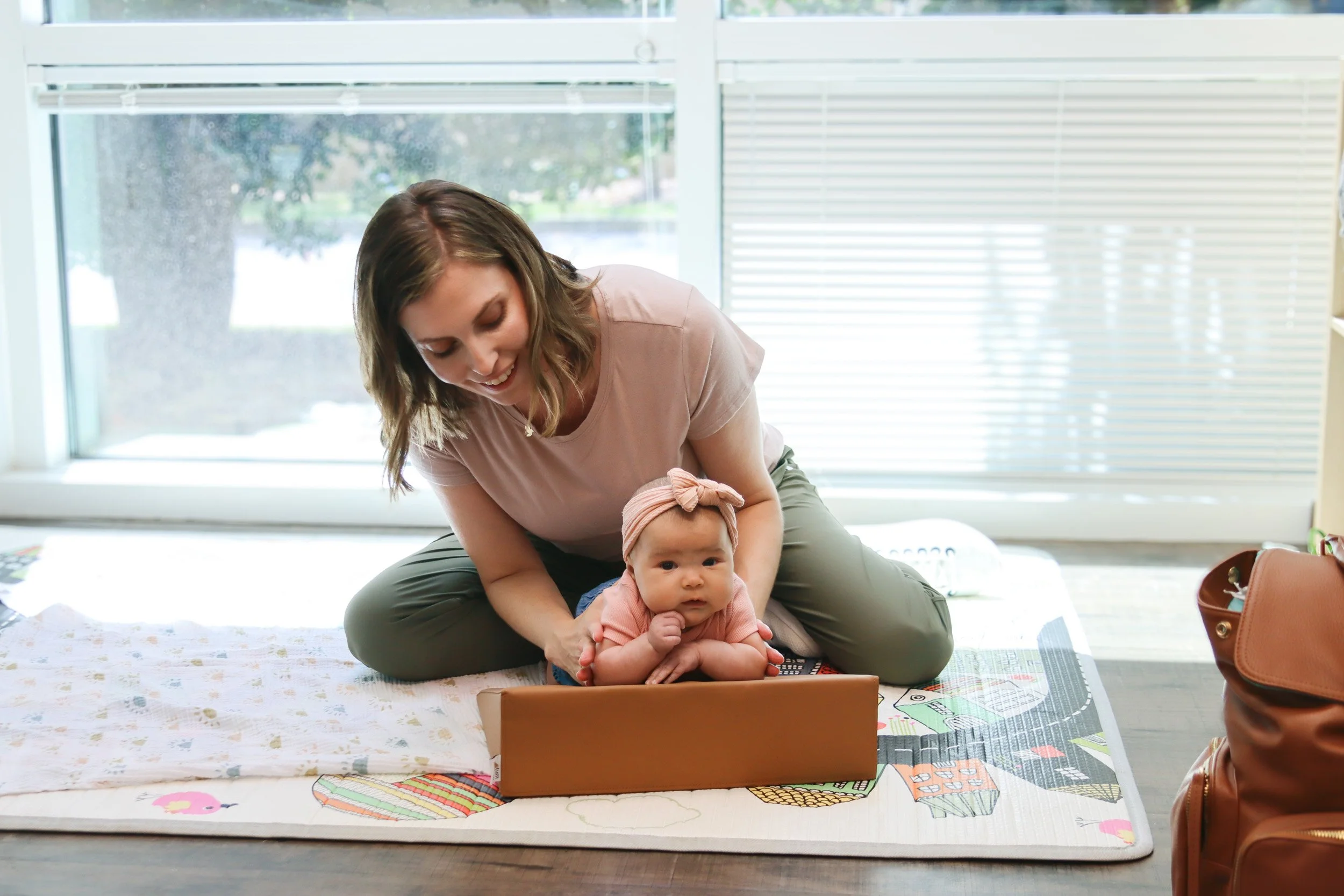 A baby girl does tummy time on an inclined surface with a pediatric physical therapist who specializes in torticollis and plagiocephaly treatment