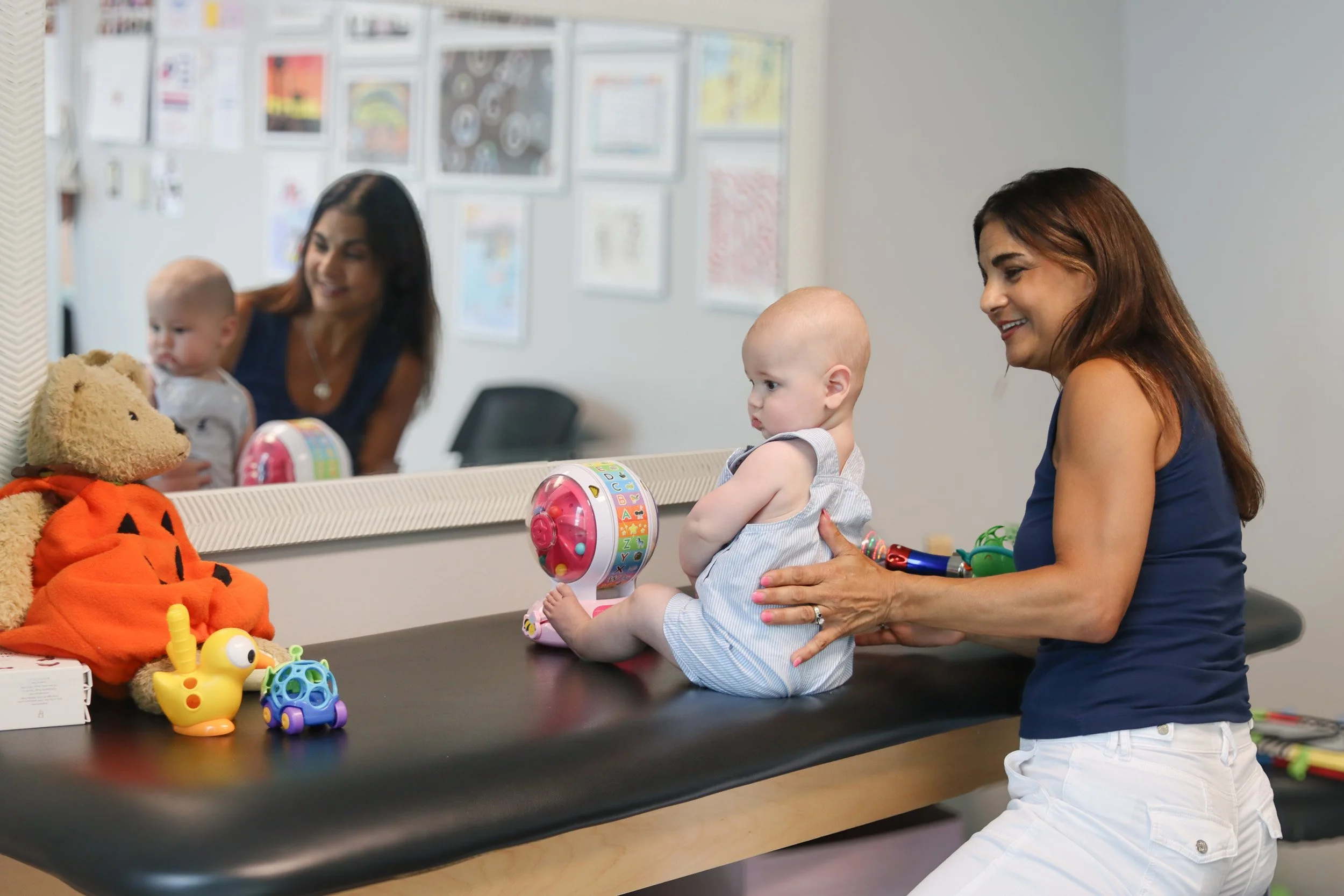 Andrea Callanen supports a baby as he sits on a table with a toy in front of a mirror at Looking Ahead's Franklin, TN office