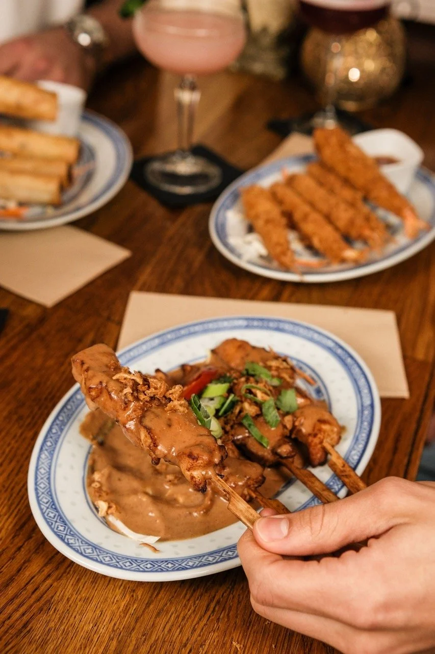 A pink cocktail garnished with orange slices, a glass of white wine, and a plate of fried food on a wooden table.