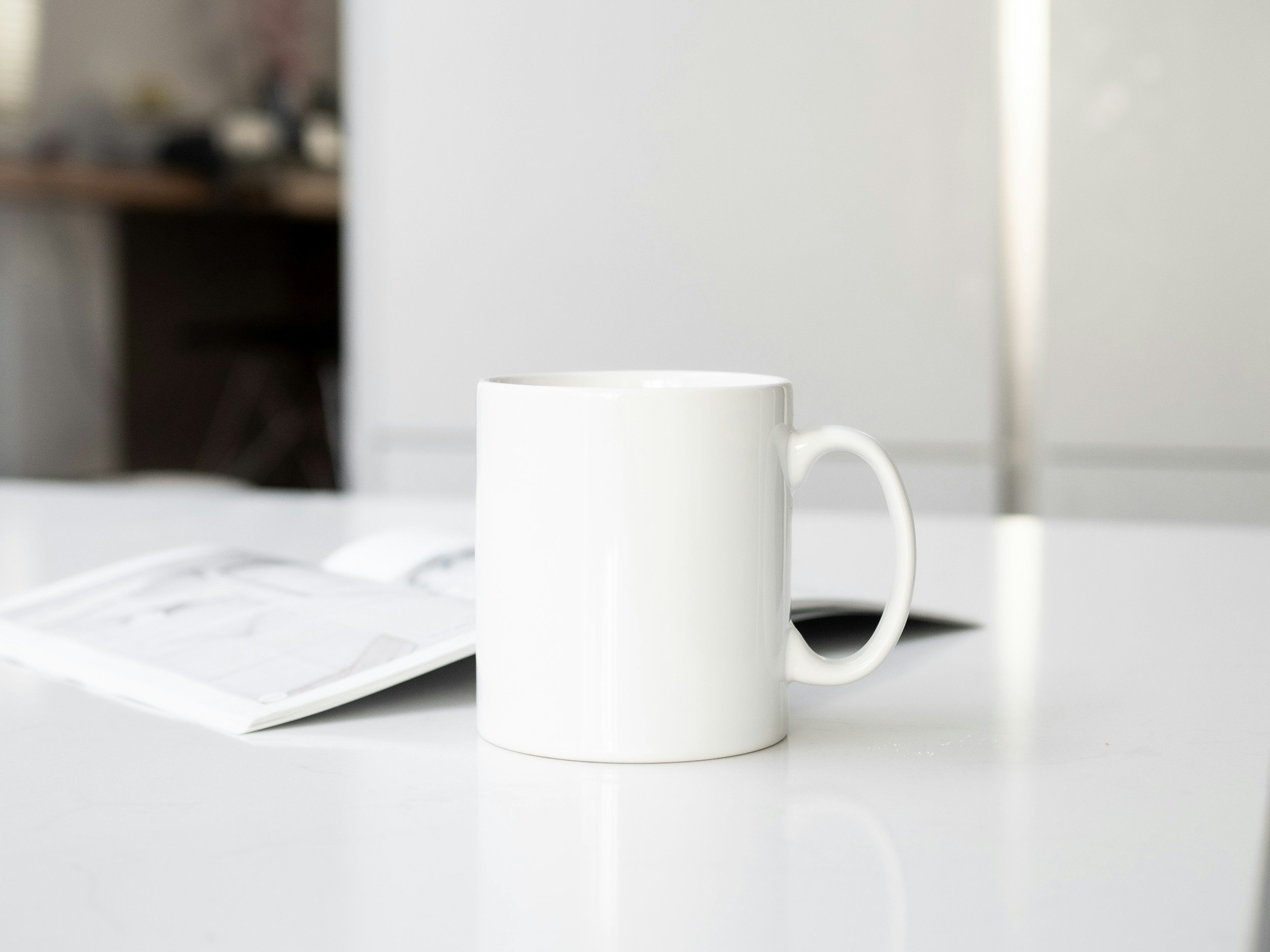 Plain white ceramic mug on a white table with an open coffee packet next to it.