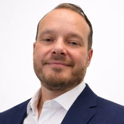 Portrait of a man in a navy blazer and white shirt smiling at the camera.