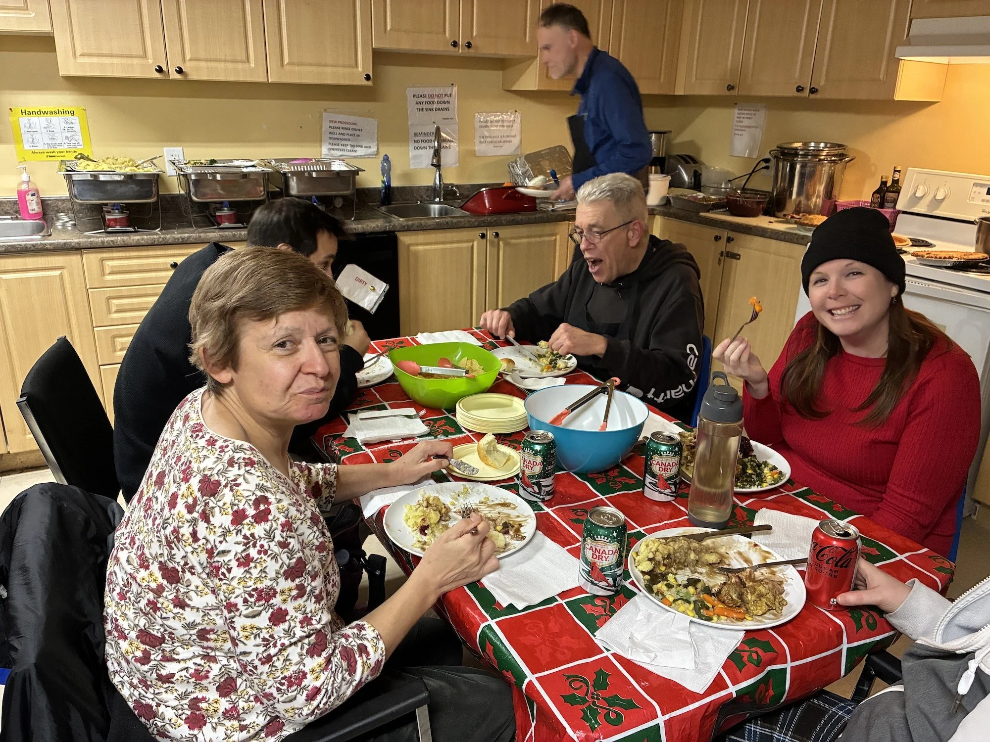 People eating and enjoying a holiday meal at a decorated table in a kitchen.
