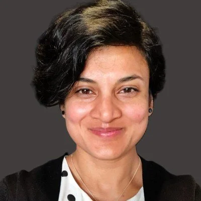 A woman with short black hair and a friendly smile, wearing a black top and a white polka dot shirt, against a gray background.