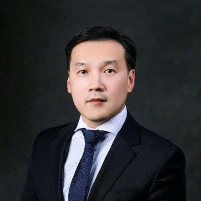 Professional headshot of a man in a suit against a dark background.