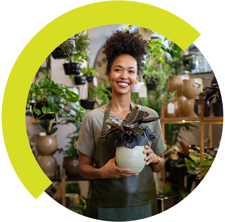 A woman smiling while holding a potted plant in a plant shop.