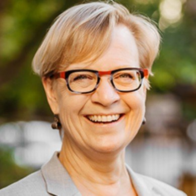 A smiling woman with short blonde hair and glasses outdoors.
