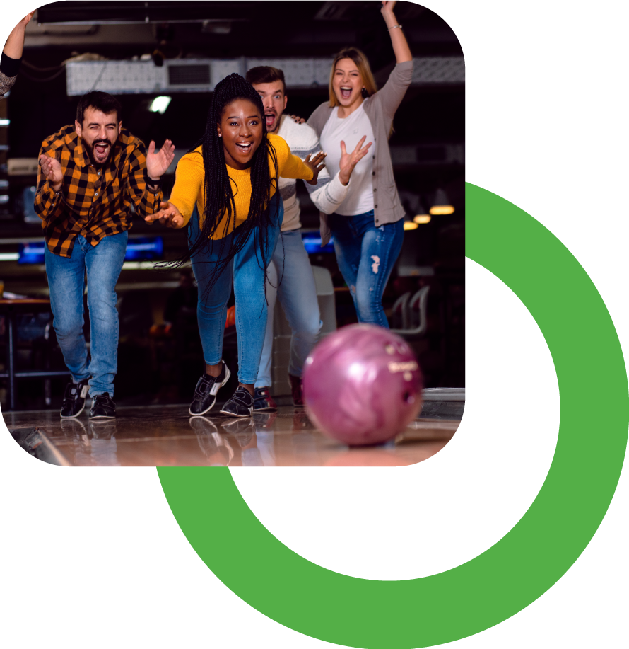 Four friends excitedly watch a bowling ball roll down the lane at a bowling alley.
