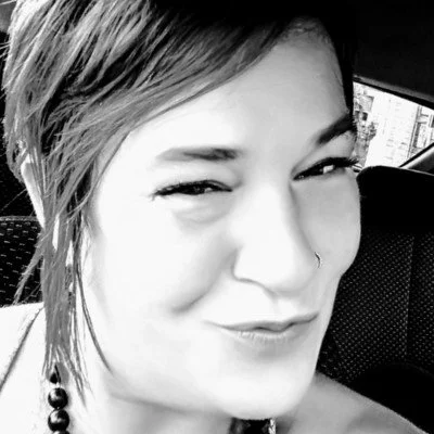 Close-up of a woman with short hair, smiling with a slight tilt of her head, in black and white.