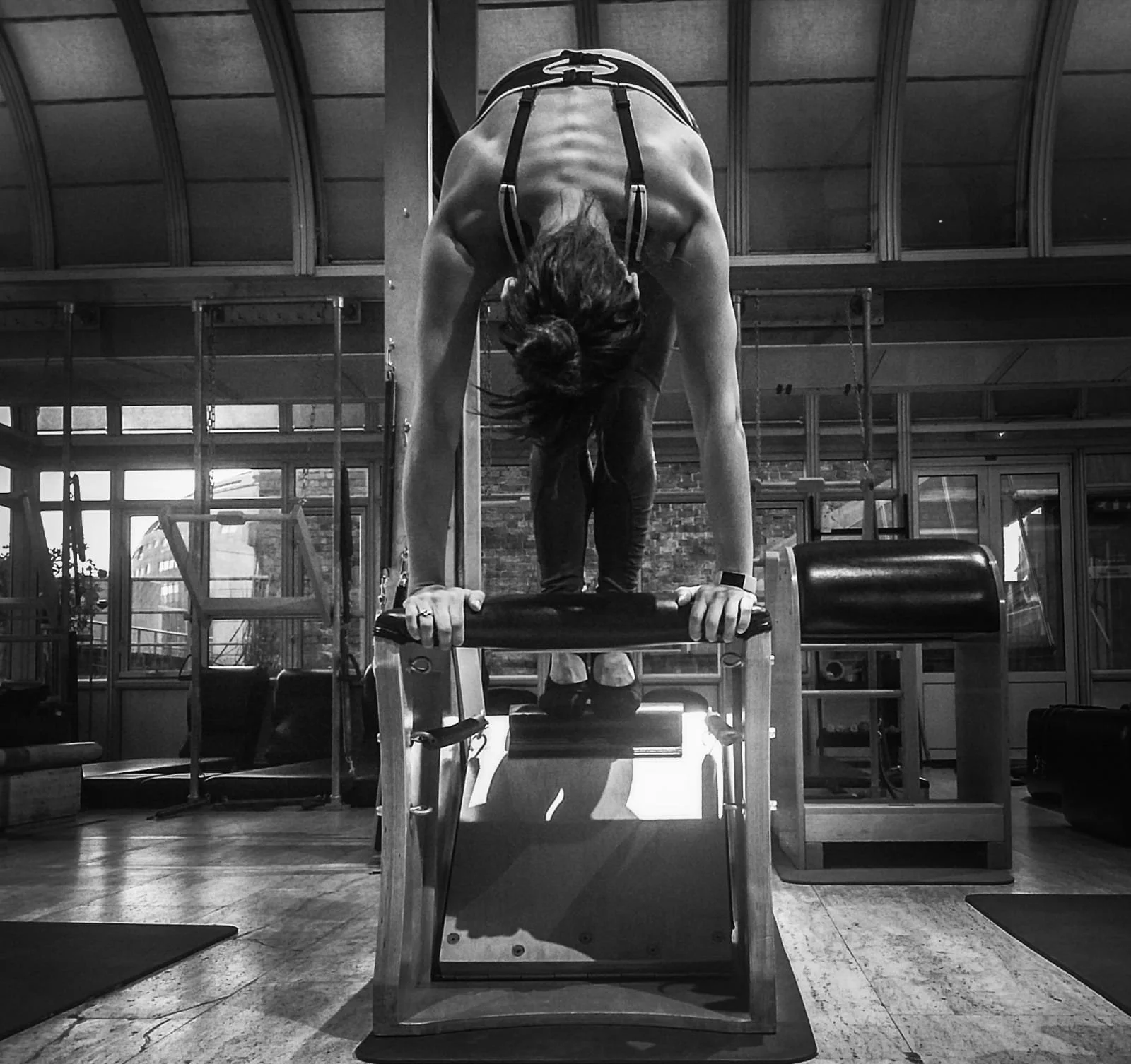 A woman in workout attire performing a handstand on parallel bars in a gym.