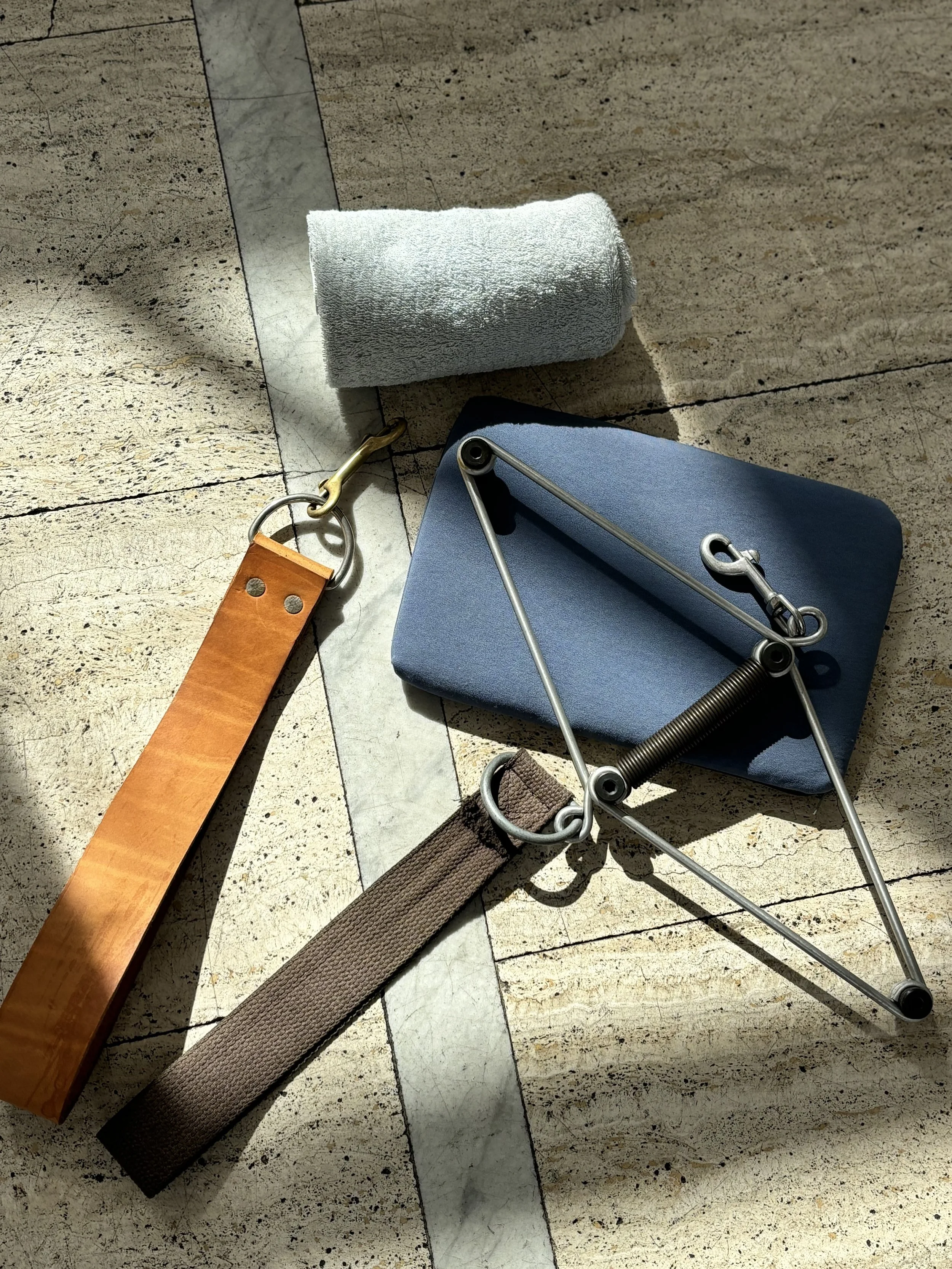 A foam roller, a hand exerciser, and a towel on a tiled floor.