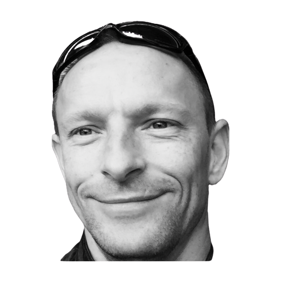 Headshot of a smiling man with short dark hair, light skin, wearing a dark hoodie, against a plain gray background.