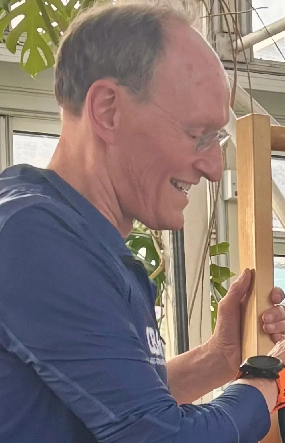 Smiling man wearing sunglasses and a blue triathlon shirt with 'SMELT GBR' written on it, outdoors on a partly cloudy day.