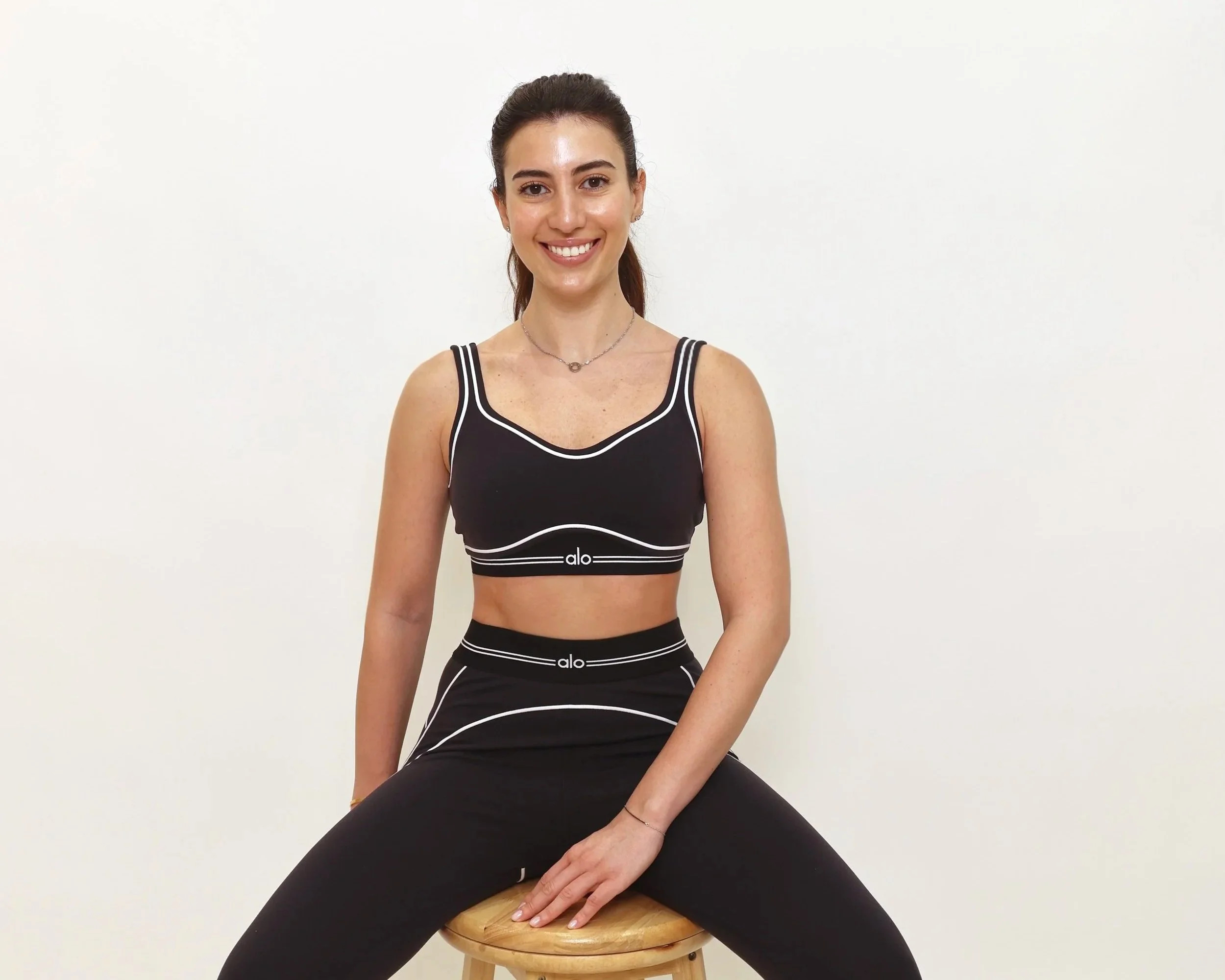 Bright, strong, fit smiling woman sitting on stool in black and white fitness wear