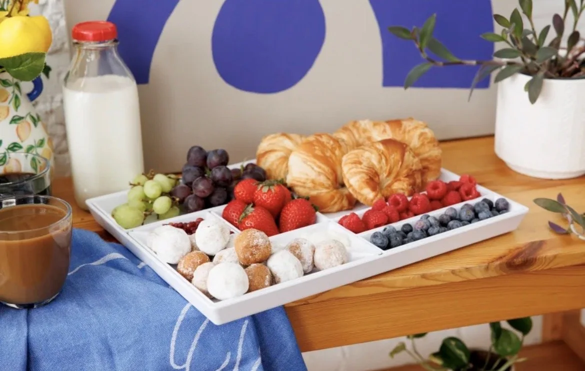 Tray with assorted fresh fruits and baked goods on a wooden table