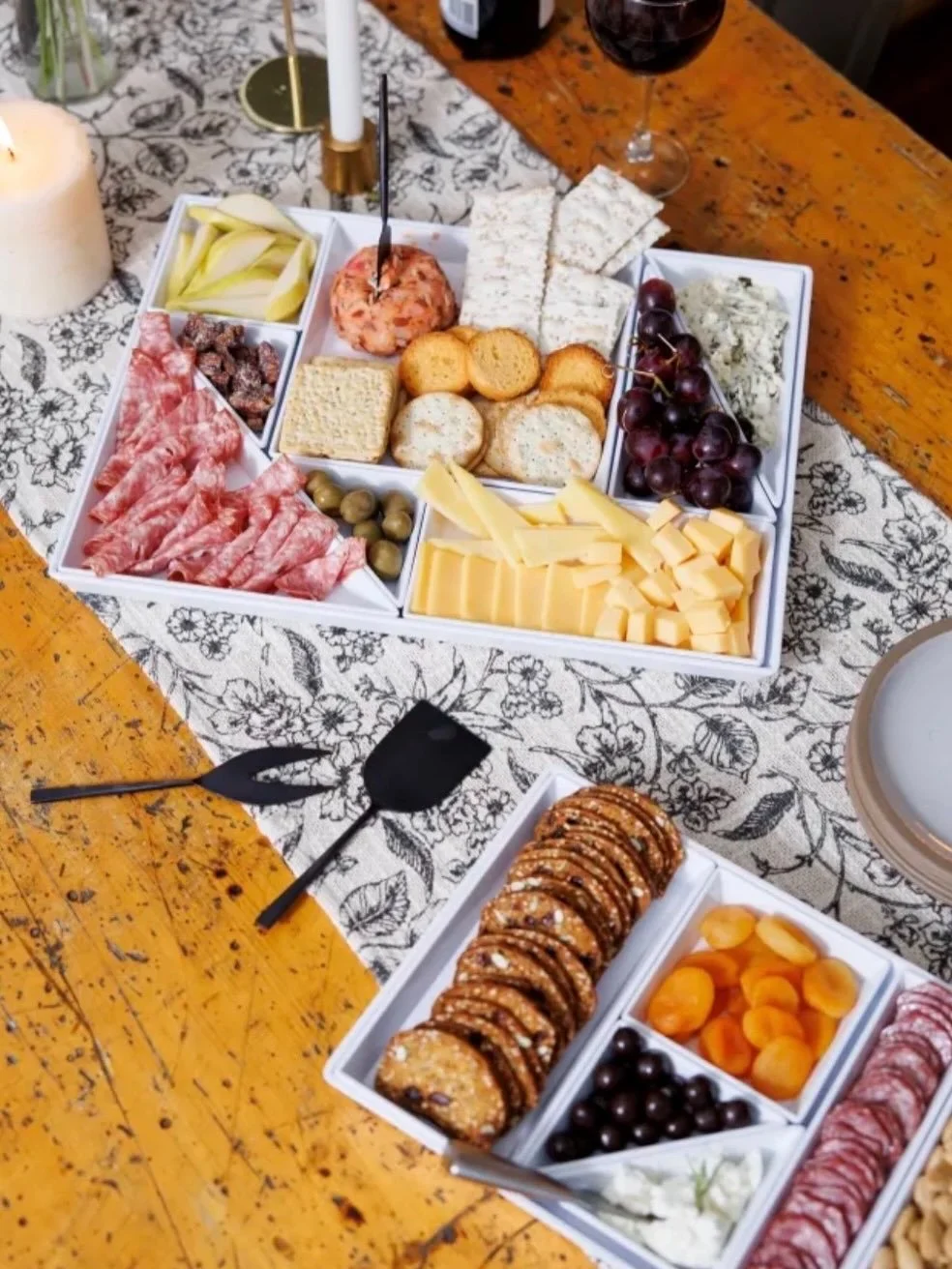 Charcuterie board with cheese, grapes, crackers, meats, and dips on a wooden table.