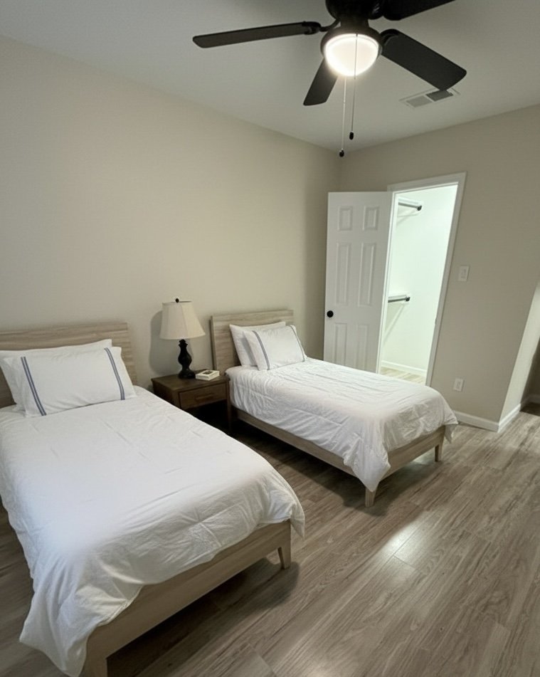 A bedroom with two twin beds, a nightstand with a lamp and a telephone, a ceiling fan, and an open door leading to a bathroom or closet with shelves.