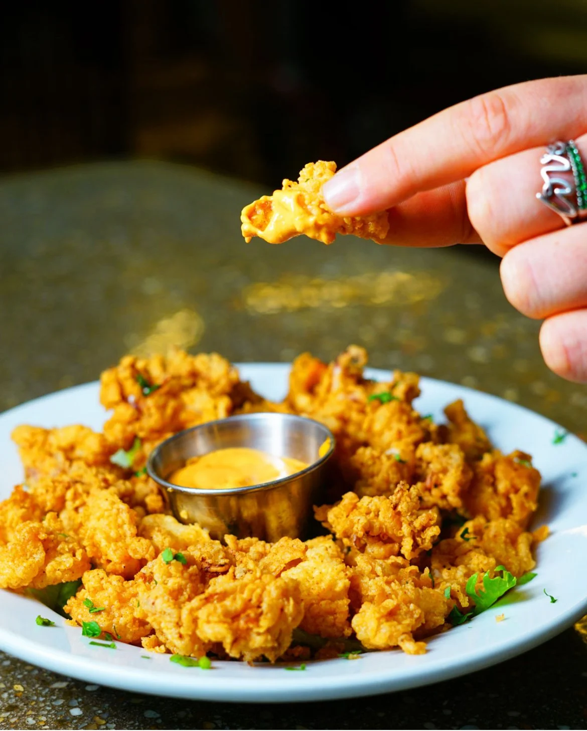 Fried chicken tenders with dipping sauce on a white plate garnished with green herbs
