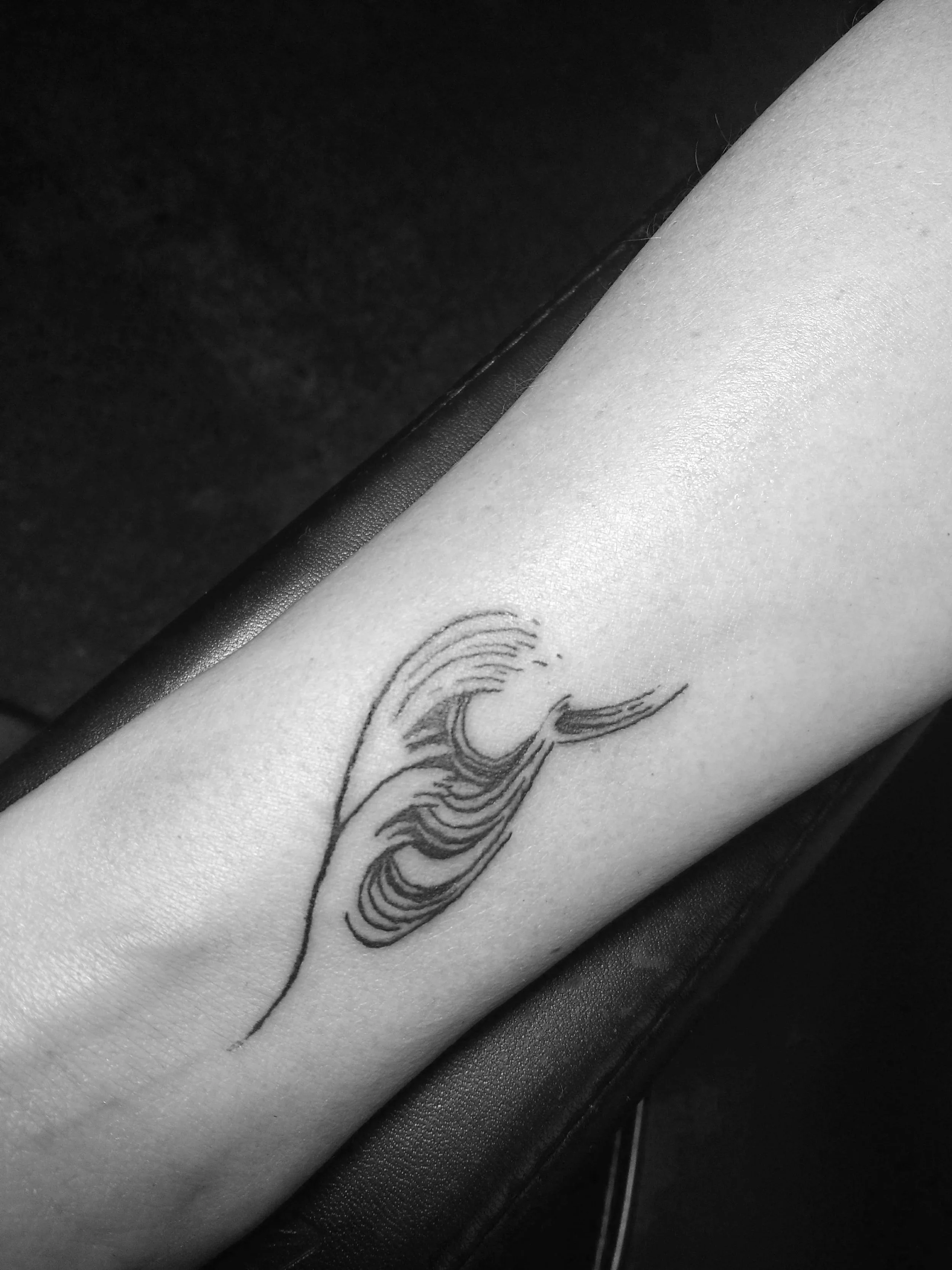 Black and white tattoo of a stylized wave on a person's forearm.
