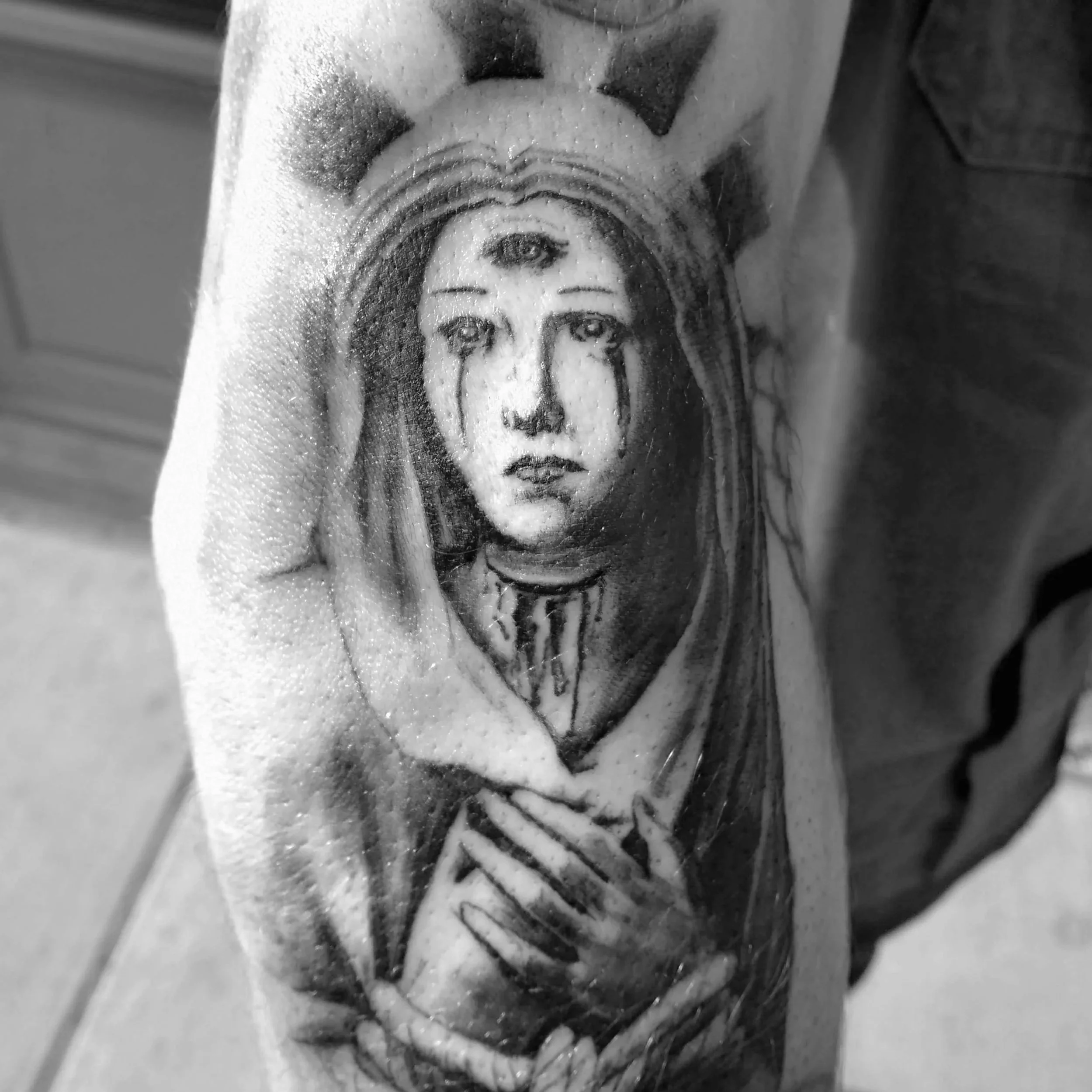 Black and white tattoo of a woman with tears on her face, wearing a crown and holding her hands over her chest.