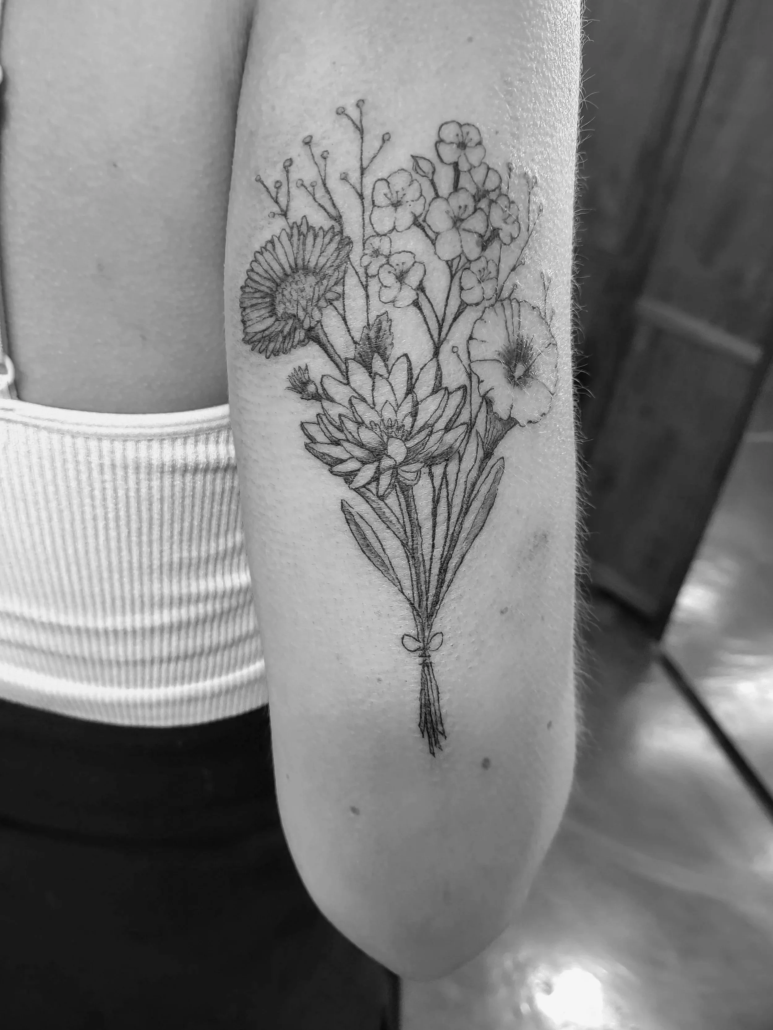 Black and white photo of a tattoo of a bouquet of flowers on a person's forearm.