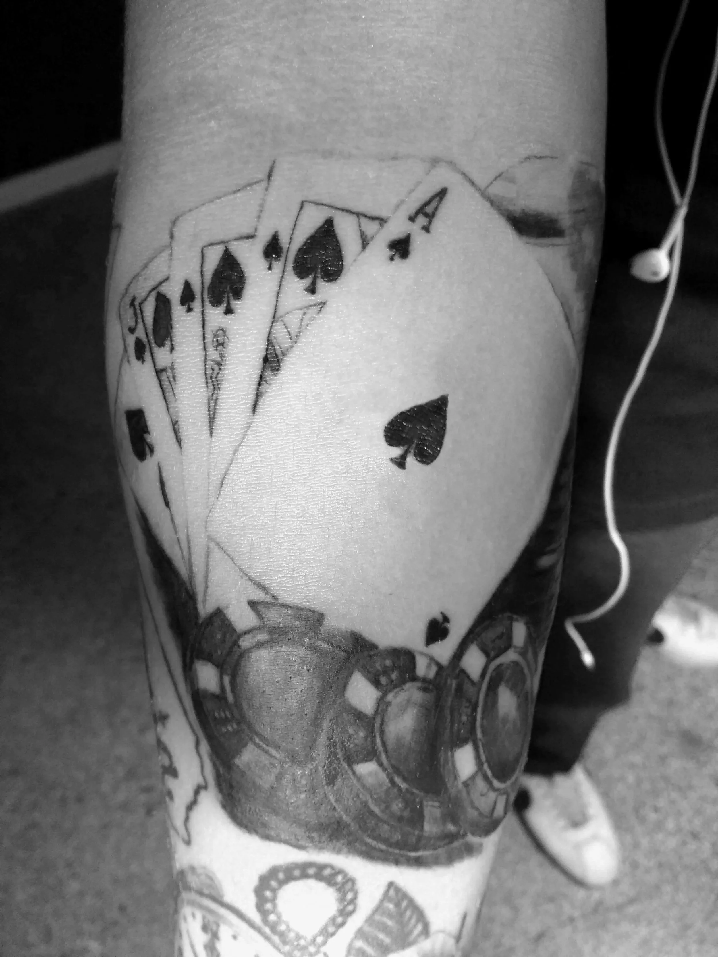 Tattoo of playing cards, poker chips, and jewelry on a person's arm.