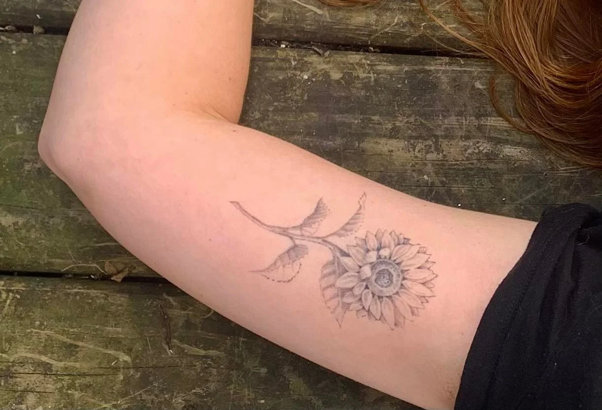 A person with a sunflower tattoo on their upper arm, lying on wooden planks.