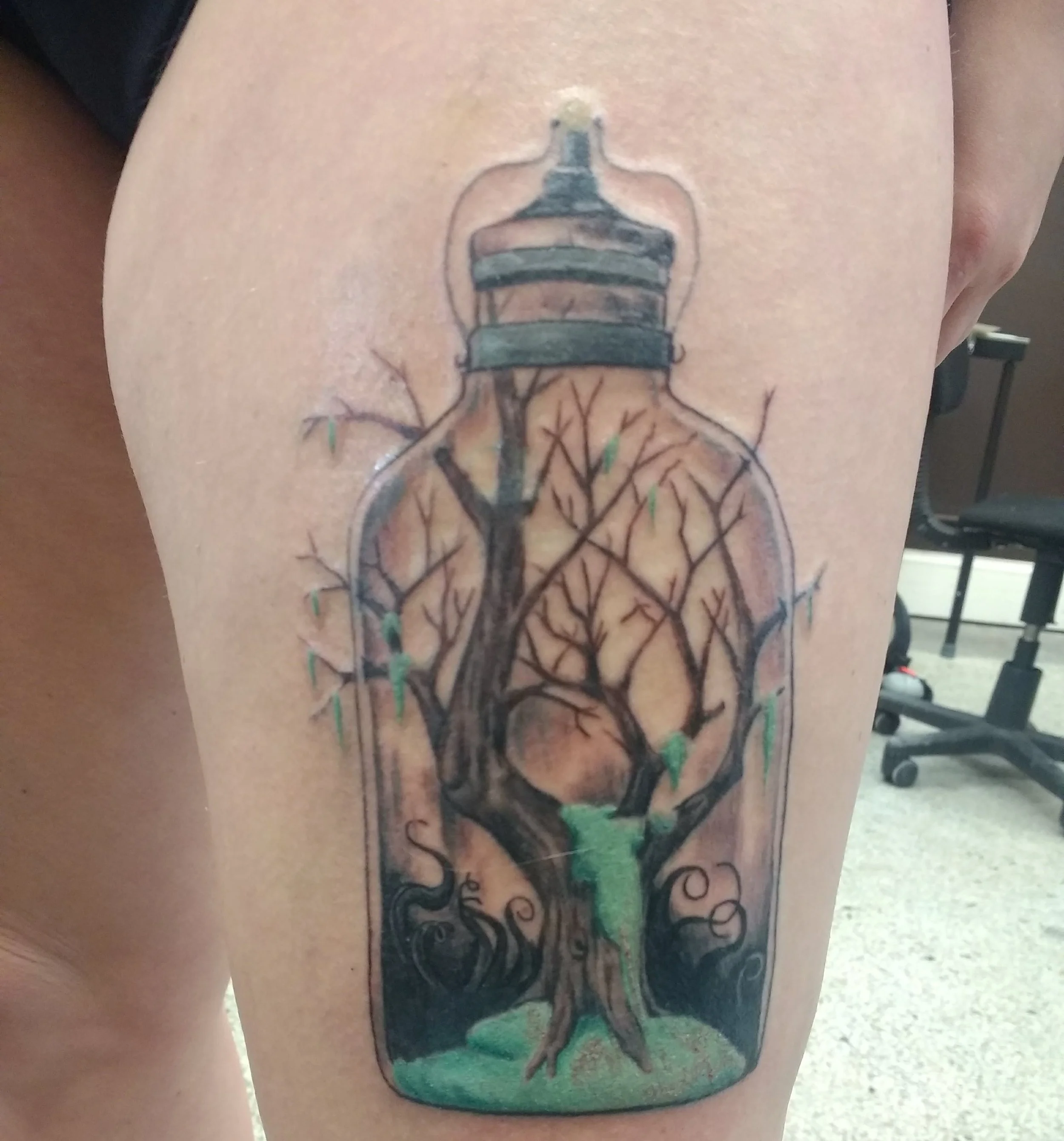 Tattoo of a tree growing inside a bottle with green leaves, roots, and a chimney on top.