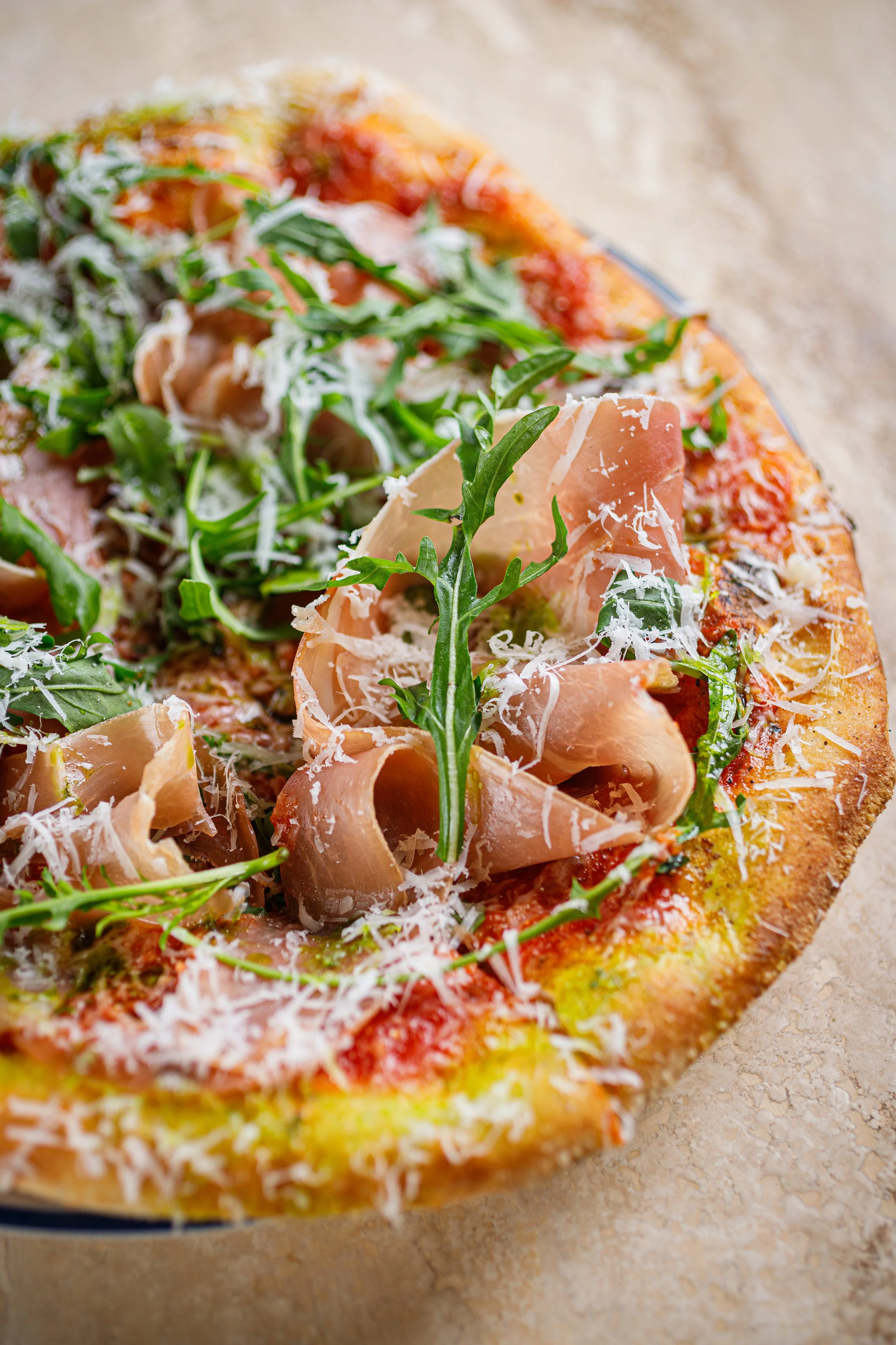 Close-up of a pizza topped with prosciutto, arugula, and grated cheese.