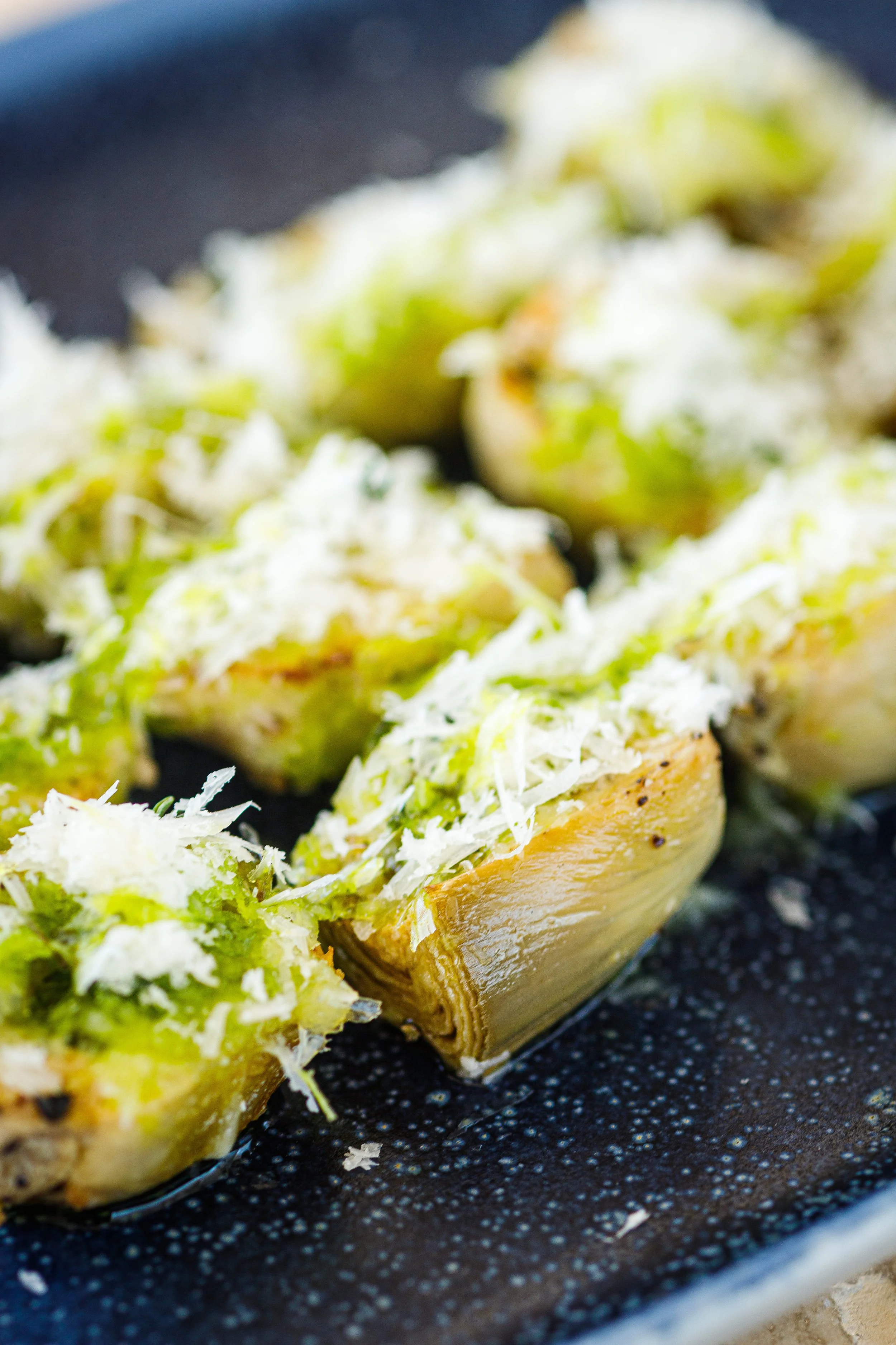 Stuffed artichoke halves topped with grated cheese on a black plate.
