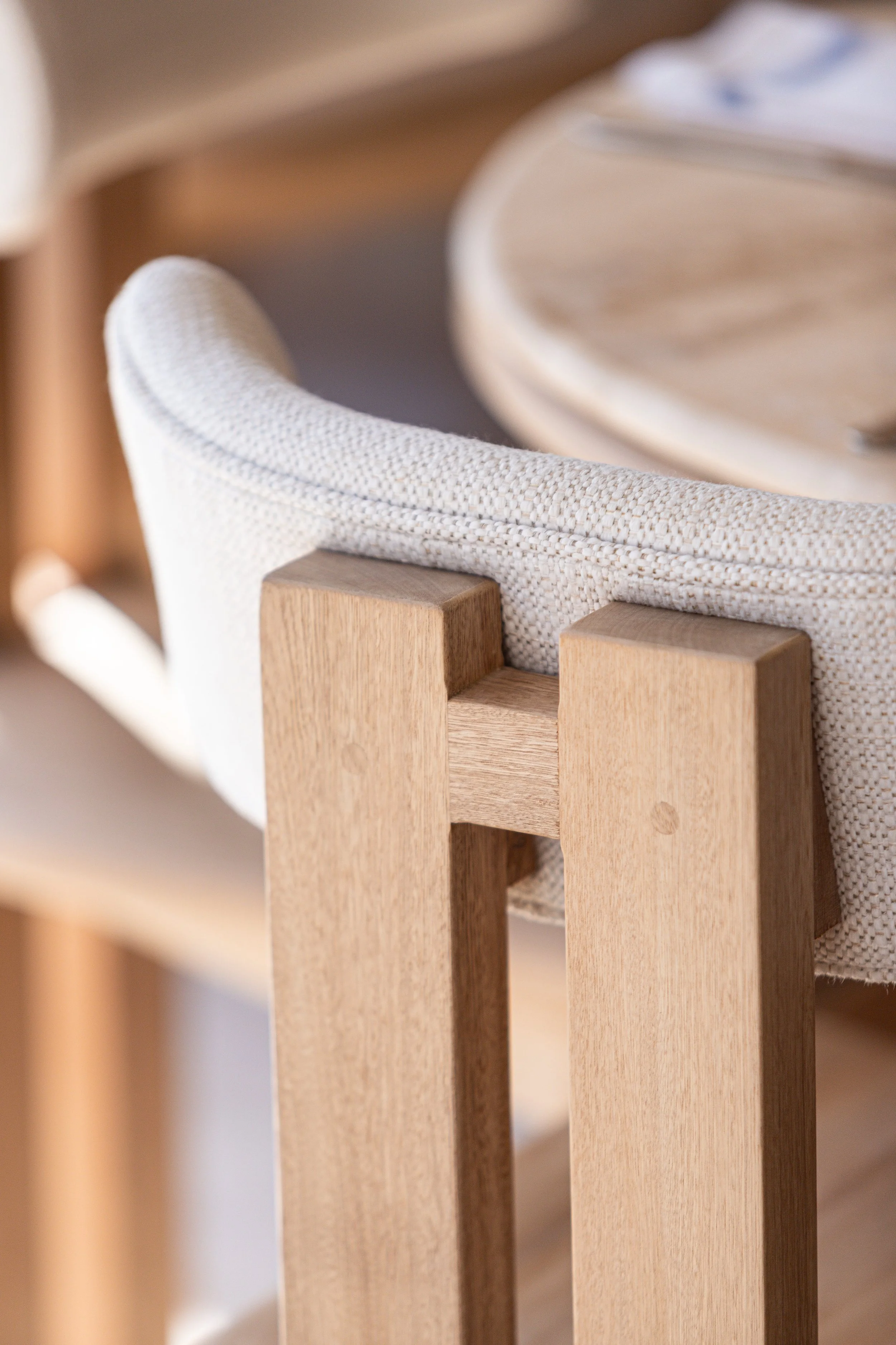 Close-up of a beige upholstered chair with wooden support at a dining table.