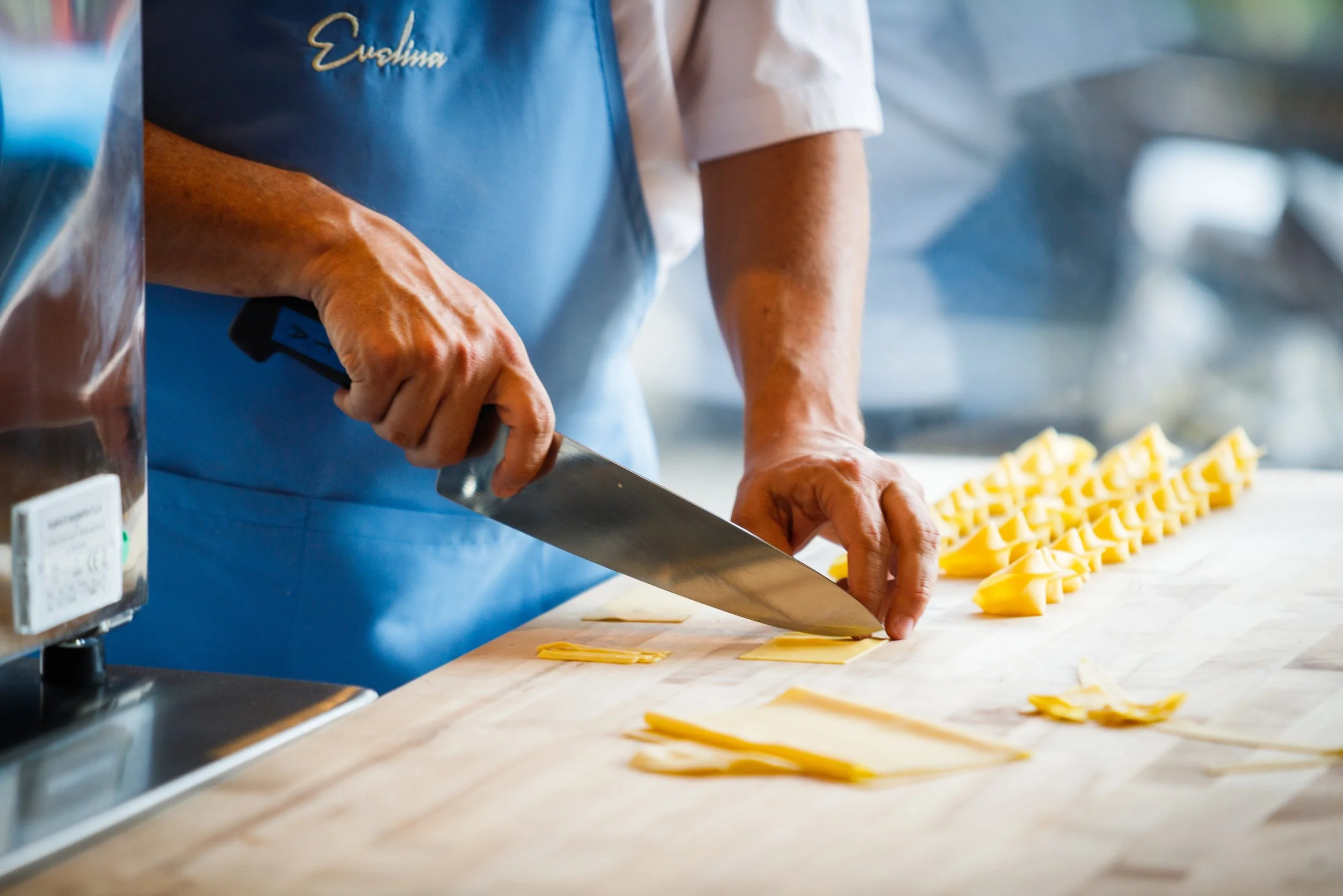 Person slicing yellow pasta on a wooden surface, wearing a blue apron.