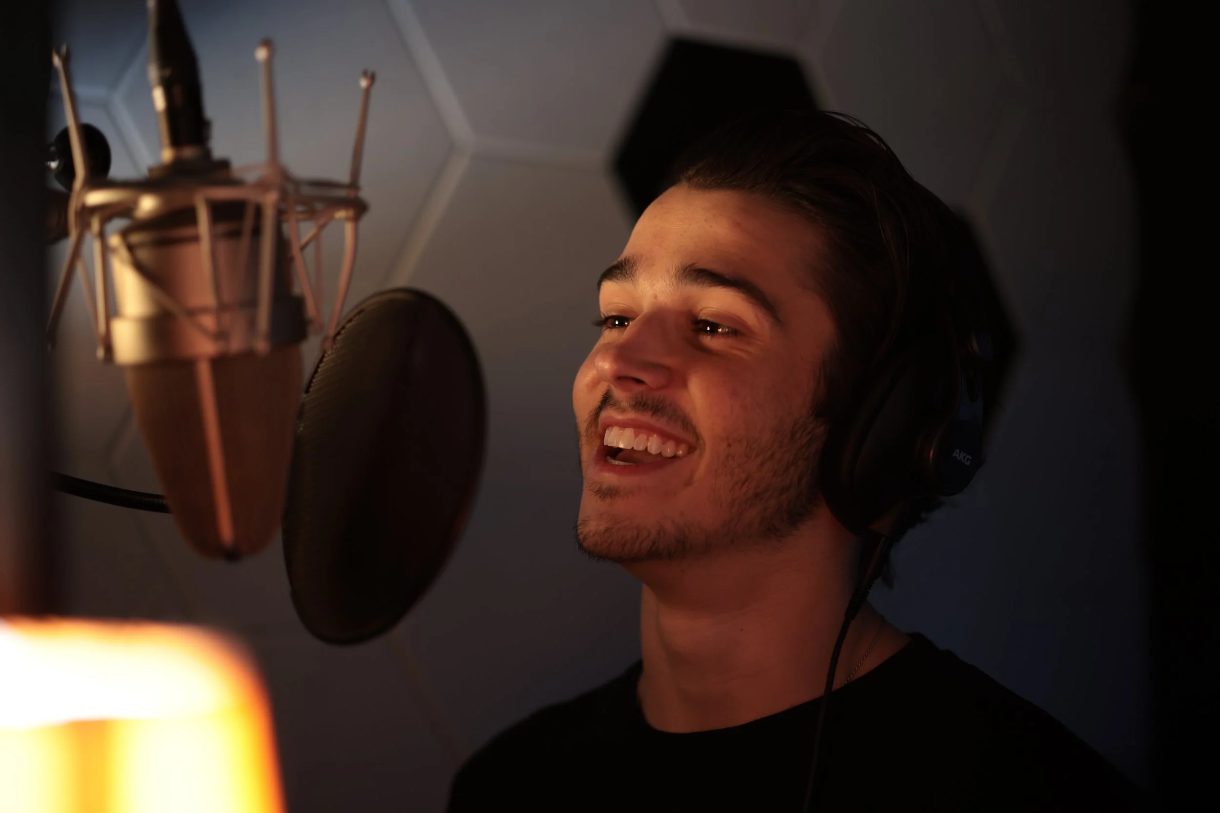 Young man singing in a recording studio with headphones and a microphone.