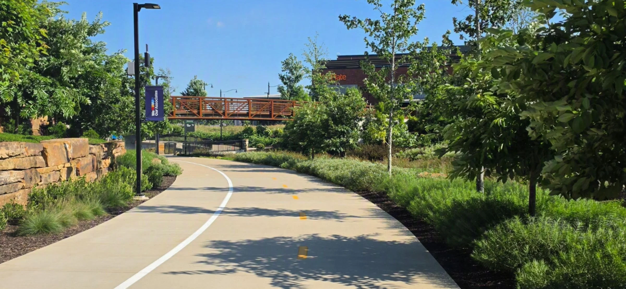 A picture of the Razorback Greenway with a brown bridge overhead used to connect between buildings while the trail flows underneath