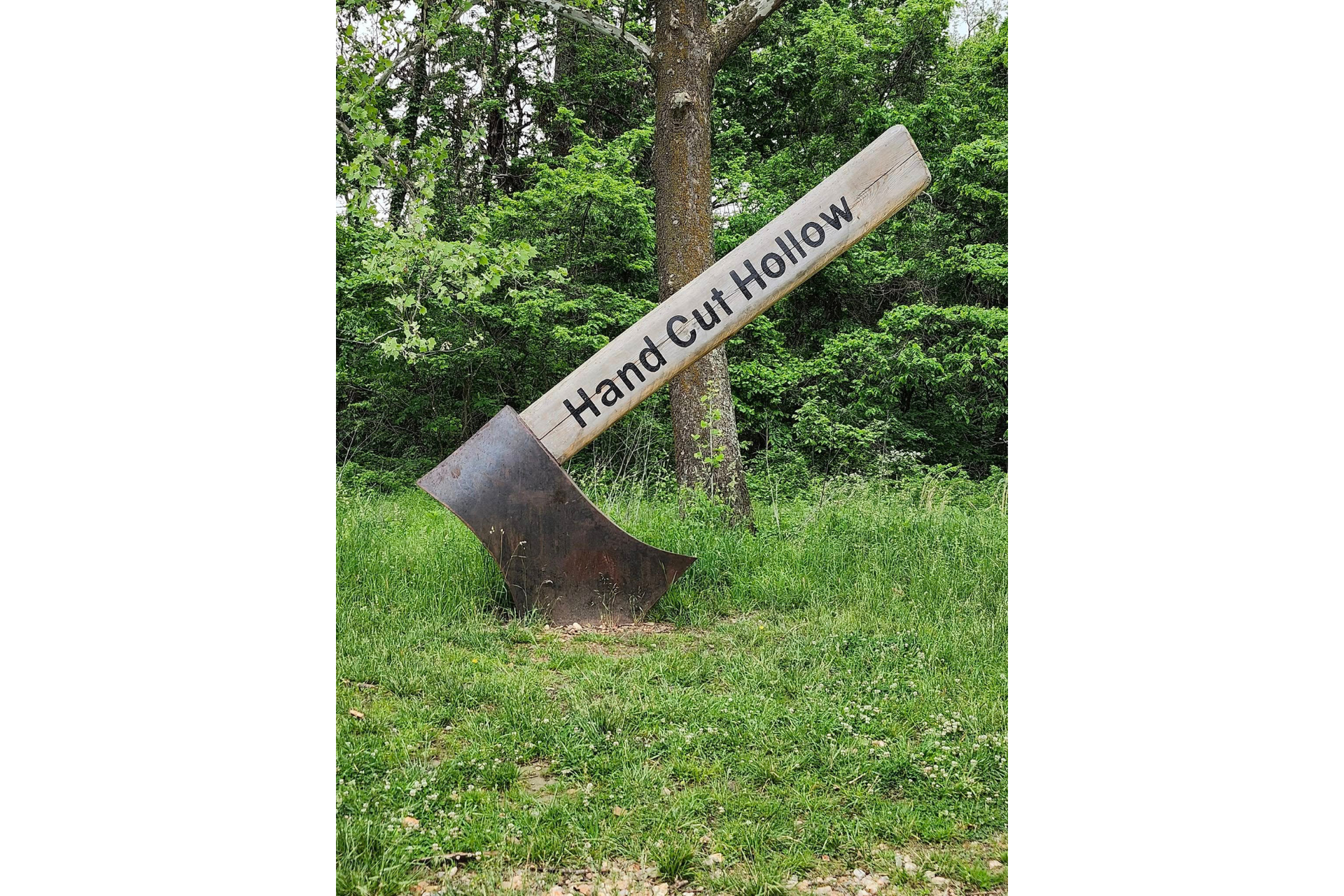 A picture of a giant ax buried in the ground with the inscriptions Handcut Hollow. This ax is found near the parking lot by Handcut Hollow