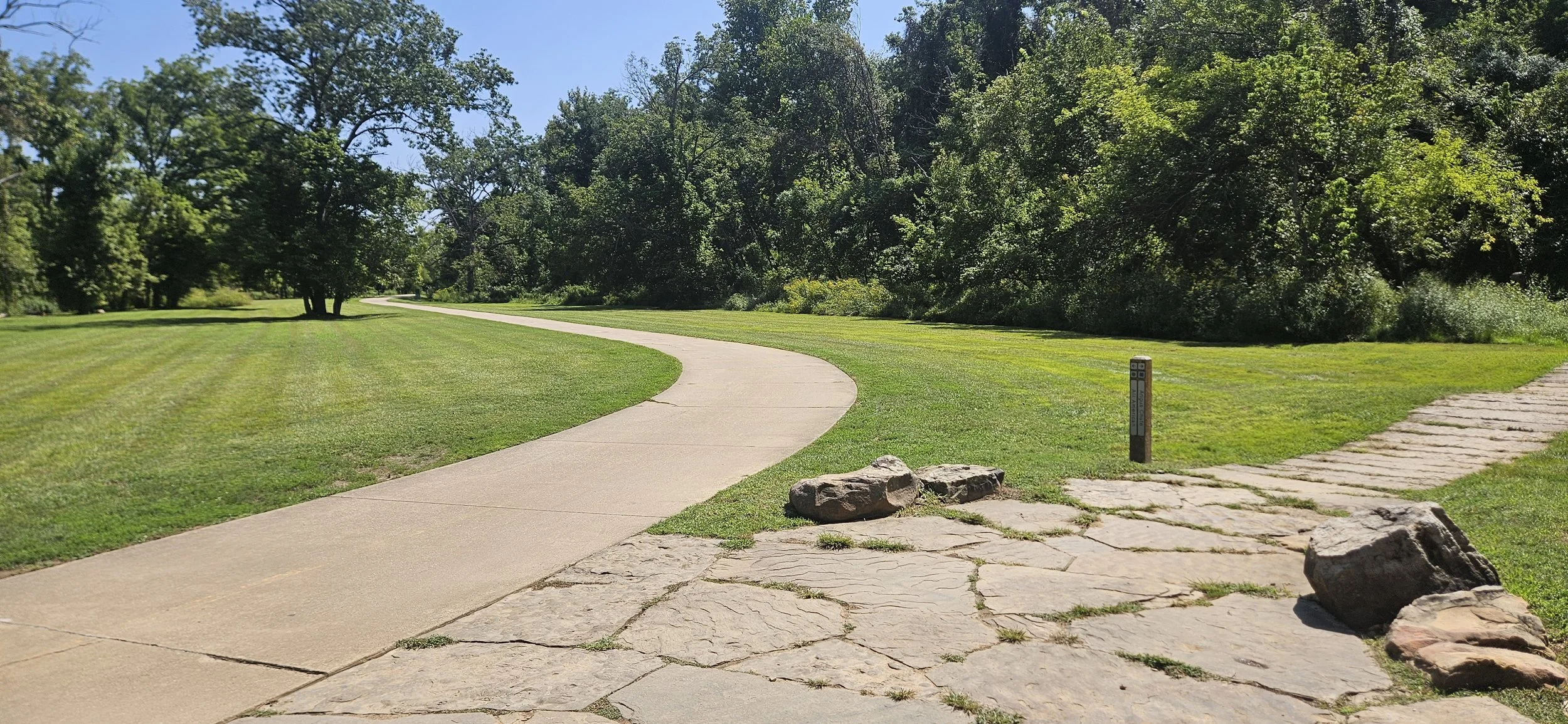 A picture of the Razorback Greenway and the signpost signifying beginning of the All American Trailhead in the Slaughter Pen trail system in Bentonville Arkansas.
