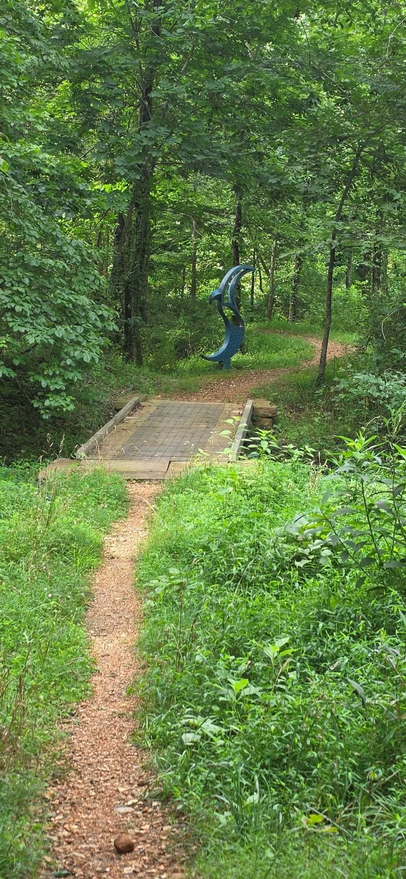 An image of a small bridge with a blue dolphin type statue in the background