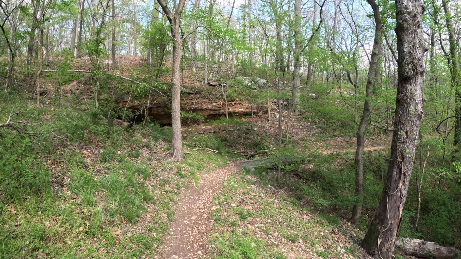 Armadillo's Last stand singletrack with a short wooden bridge that runs by an exposed Arkansas layered shale rock formation