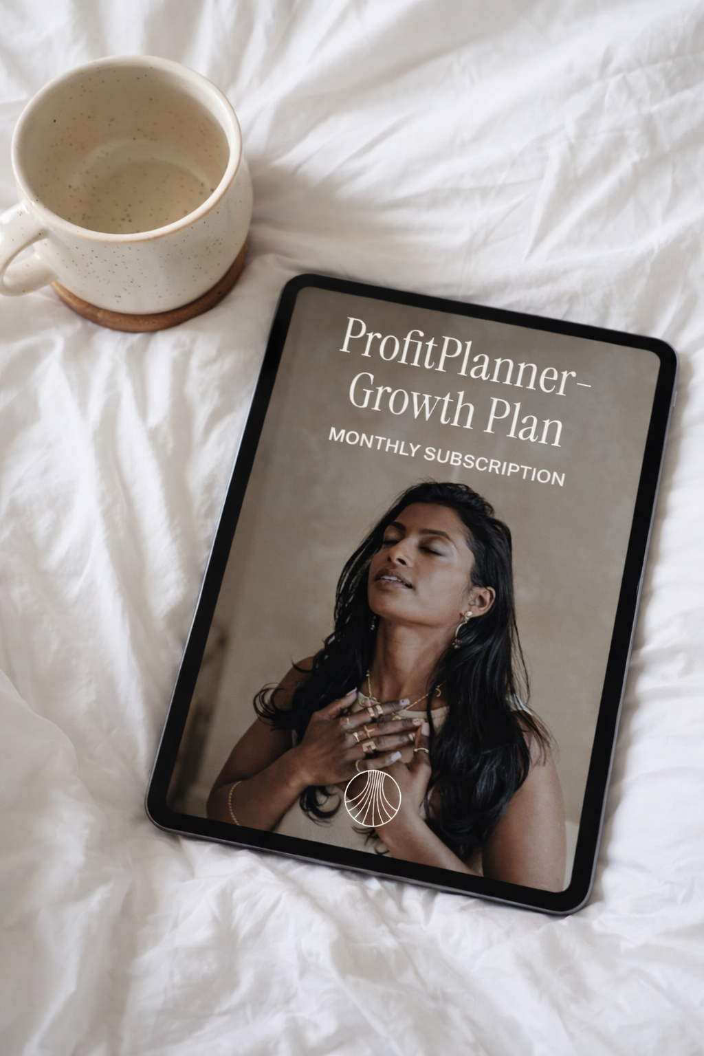 A tablet displaying a profit planner growth plan with a woman on the cover, placed on a white fabric surface next to an empty beige ceramic mug.